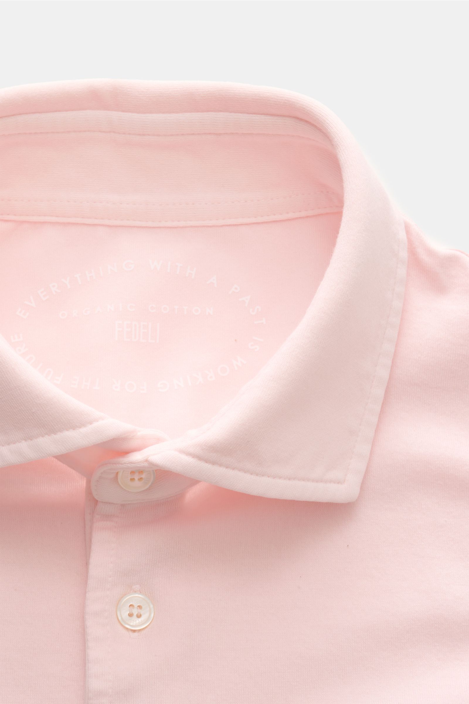 Nahaufnahme des Fedeli Jersey-Poloshirts 'Zero' rosé von oben, zeigt Haifisch-Kragen, Perlmuttknöpfe, Jersey aus Bio-Baumwolle.
