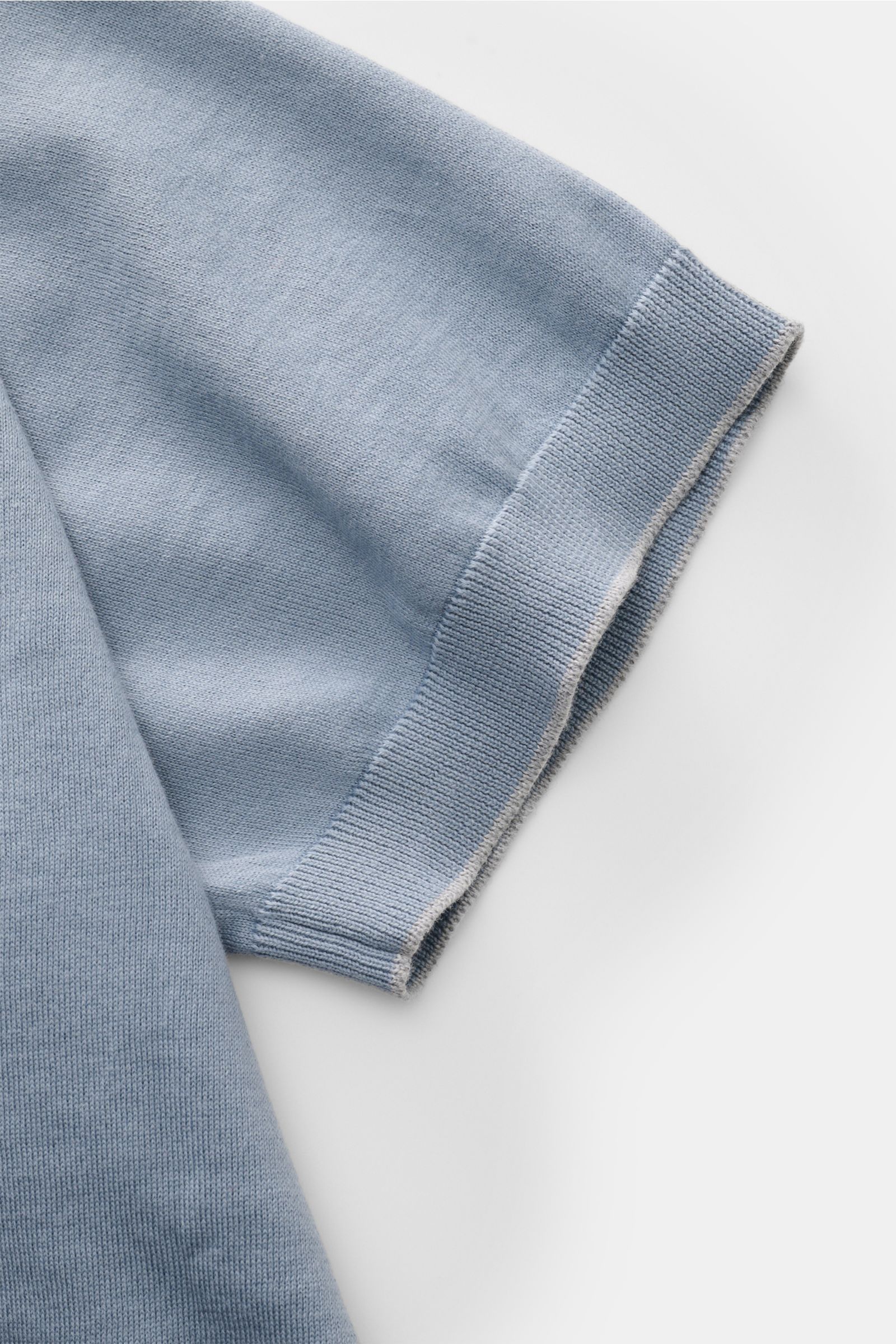 Close-up of the short sleeve on the right side of the Brunello Cucinelli Kurzarm-Strickpolo rauchblau, photographed from above on a white background, showing the fine knit cotton fabric with a soft touch, slim fit, classic polo collar, three-button placke