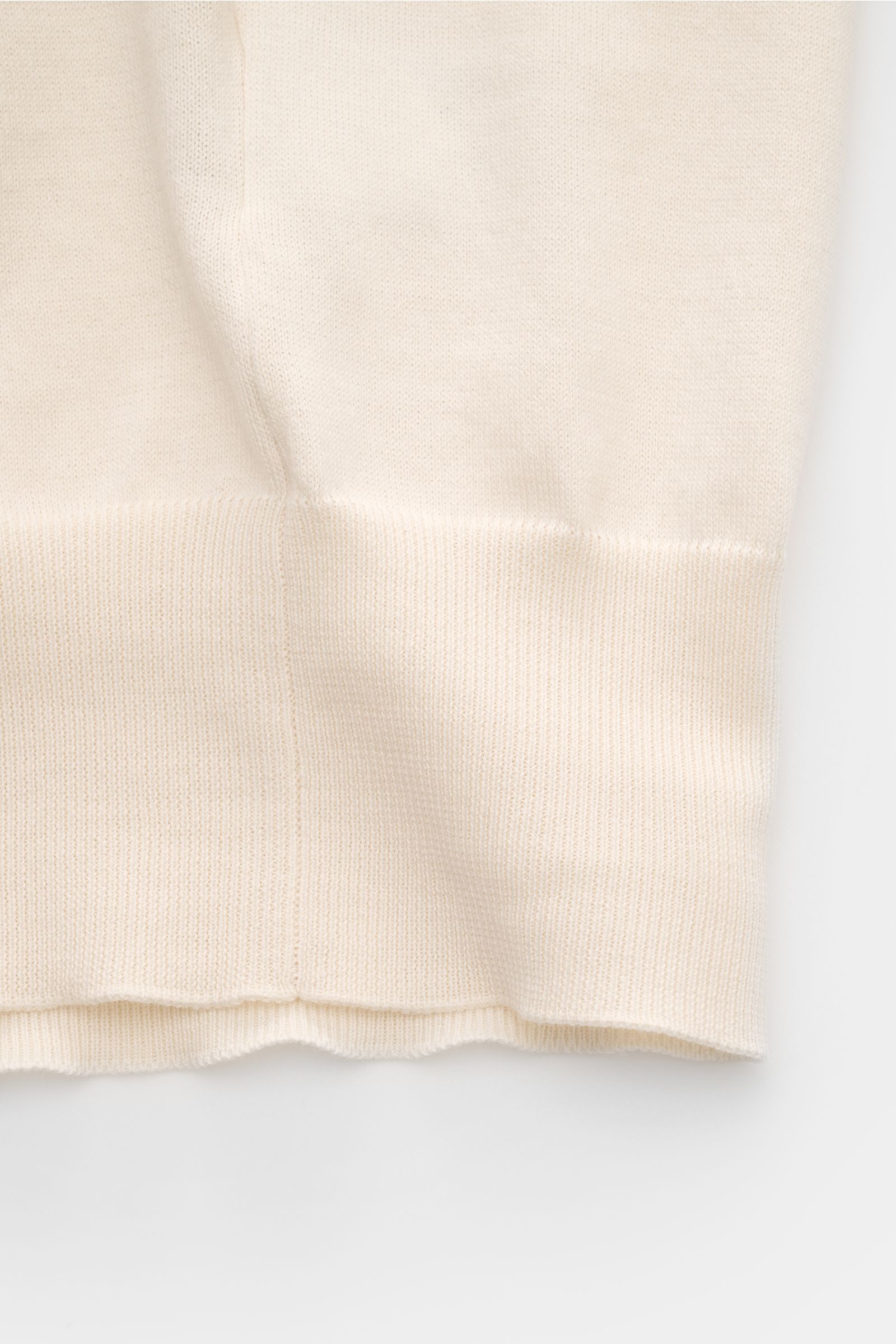 Close-up of the hem and side seam of the Brunello Cucinelli Kurzarm-Strickpolo creme, photographed from the side on a white background. Luxuriöse Alltags-Looks profitieren von der leichten Strickqualität dieses zeitlosen Kurzarm-Poloshirts von BRUNELLO CU