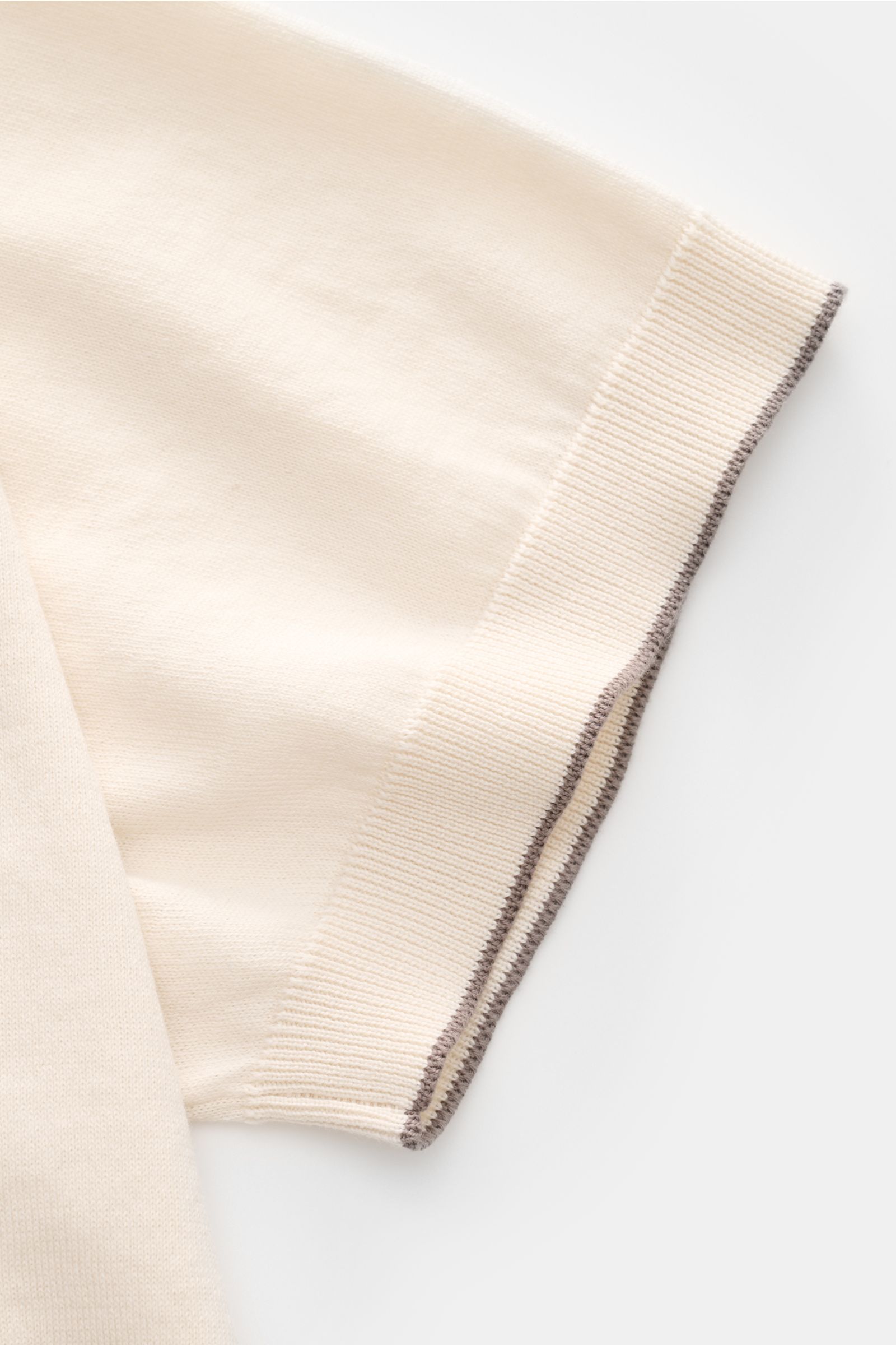 Close-up side view of the sleeve of the Brunello Cucinelli Kurzarm-Strickpolo creme, showcasing fine cotton knit, soft texture, slim fit, classic collar, three-button placket, and ribbed cuffs with contrast edges.

Luxuriöse Alltags-Looks profitieren v