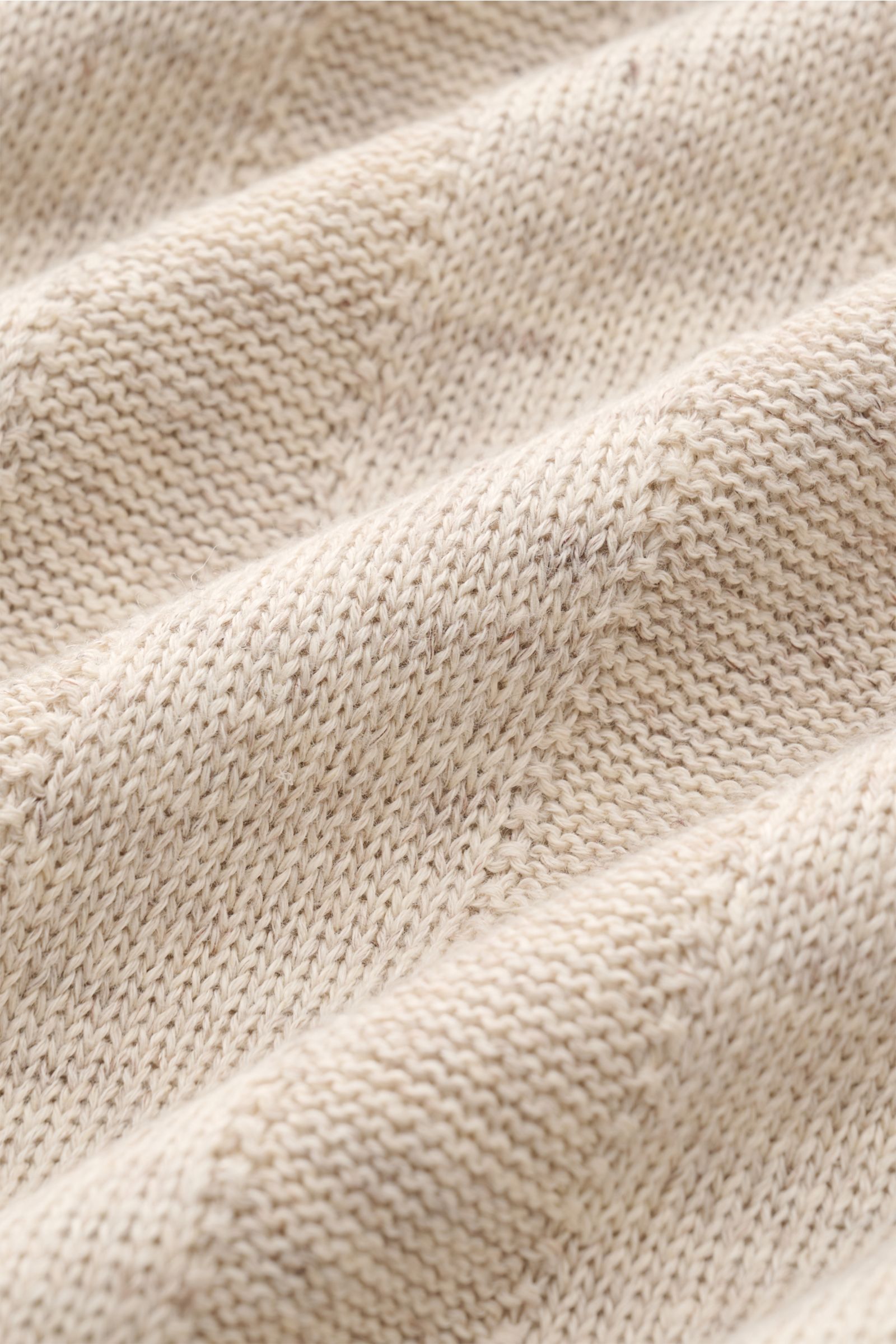 Nahaufnahme des sand melierten Strickstoffs des Brunello Cucinelli Kurzarm-Strickpolo mit mittelfeinem Streifenmuster, weichem Griff und schmalen Kontrastkanten, fotografiert aus schräger Perspektive.