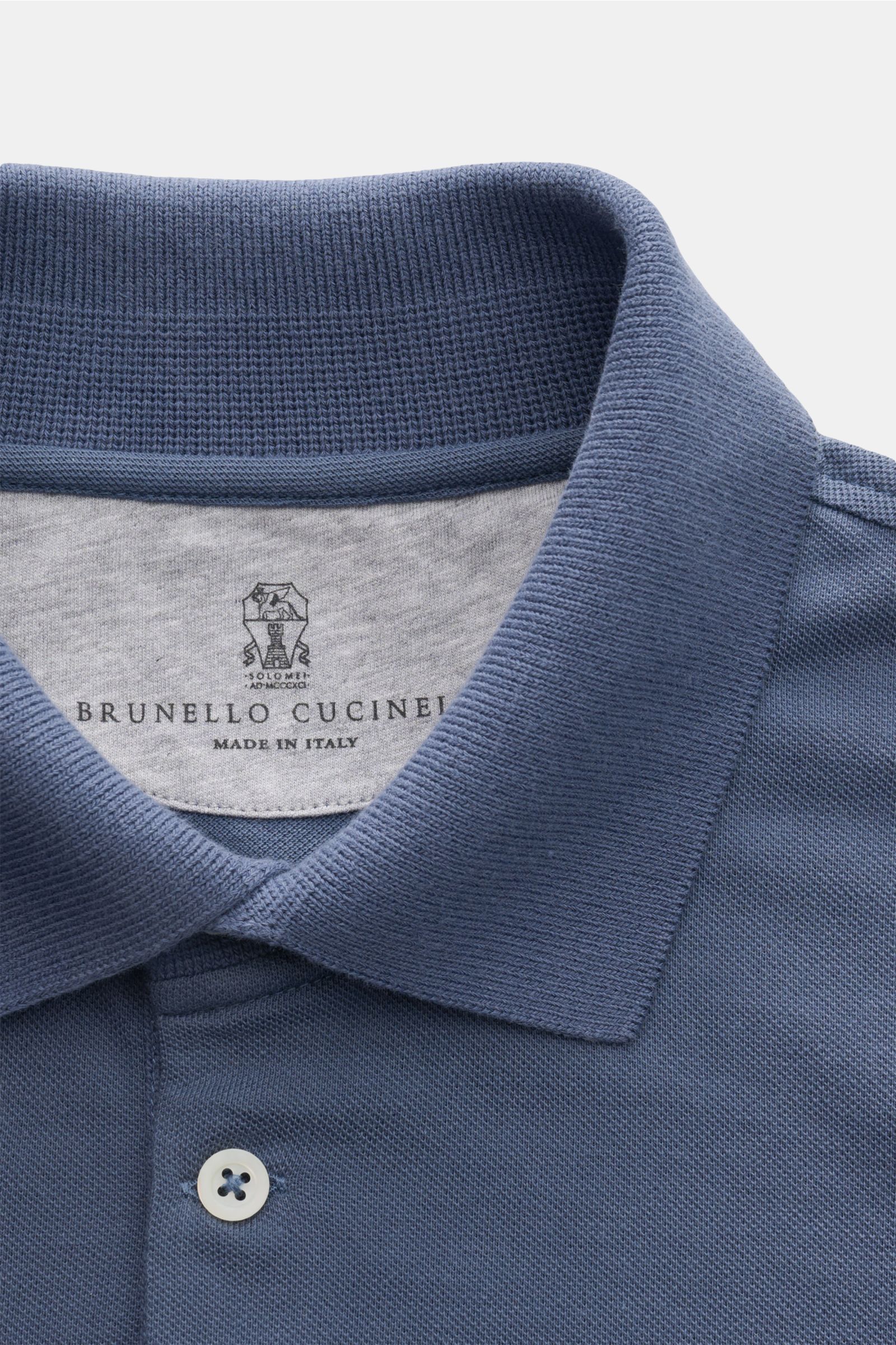 Close-up front view of a blue Brunello Cucinelli Poloshirt weiß showing the classic piqué fabric, slim fit, tailored collar, three-button placket, ribbed cuffs with contrast edge, and short hem slits. Cleanes Essential erster Wahl: Liebhaber der Luxusm