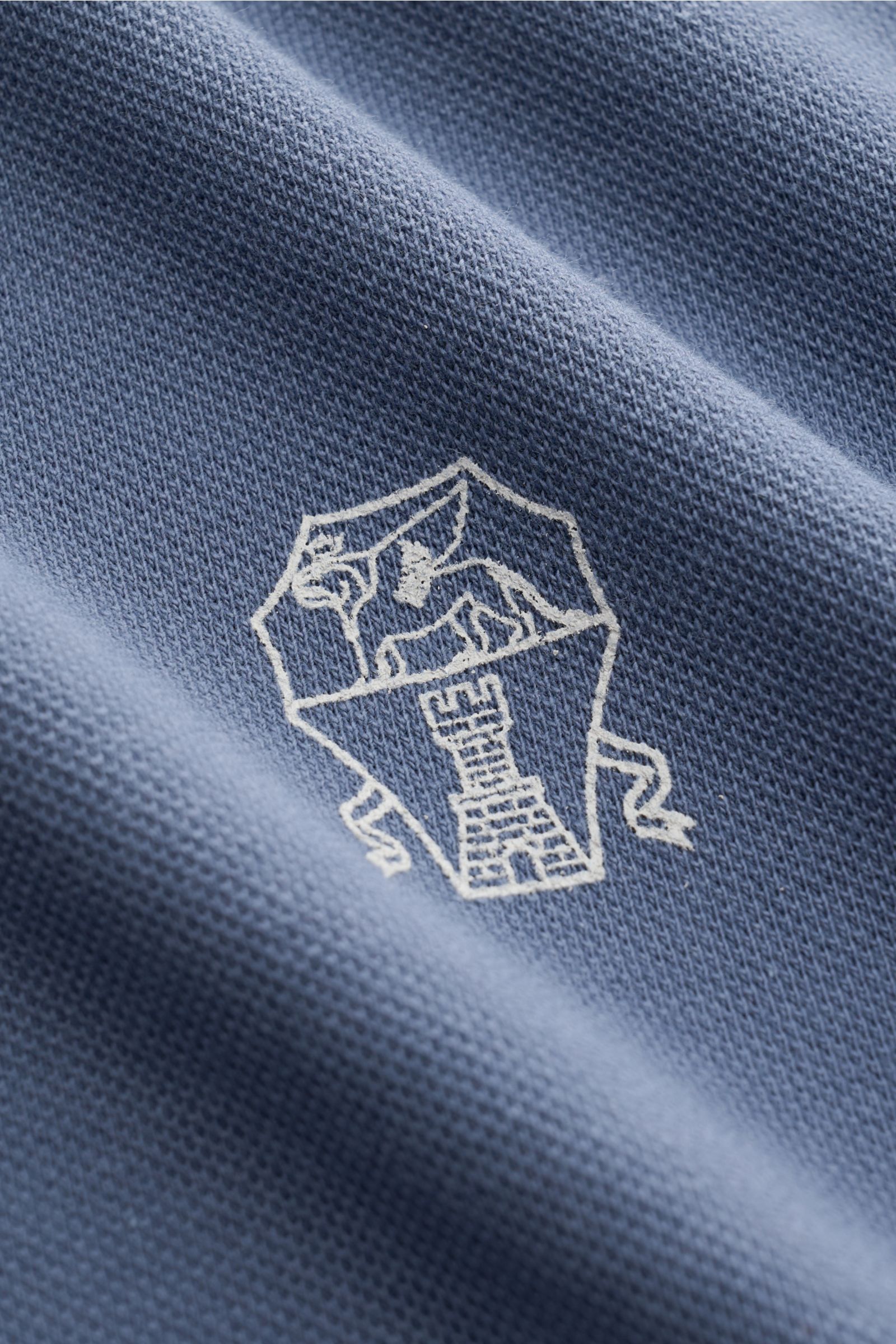 Close-up front view of a blue Brunello Cucinelli Poloshirt weiß showing the detailed white logo on classic piqué fabric. Cleanes Essential erster Wahl: Liebhaber der Luxusmarke BRUNELLO CUCINELLI sind mit diesem zeitlosen Poloshirt aus klassischem Piqué m