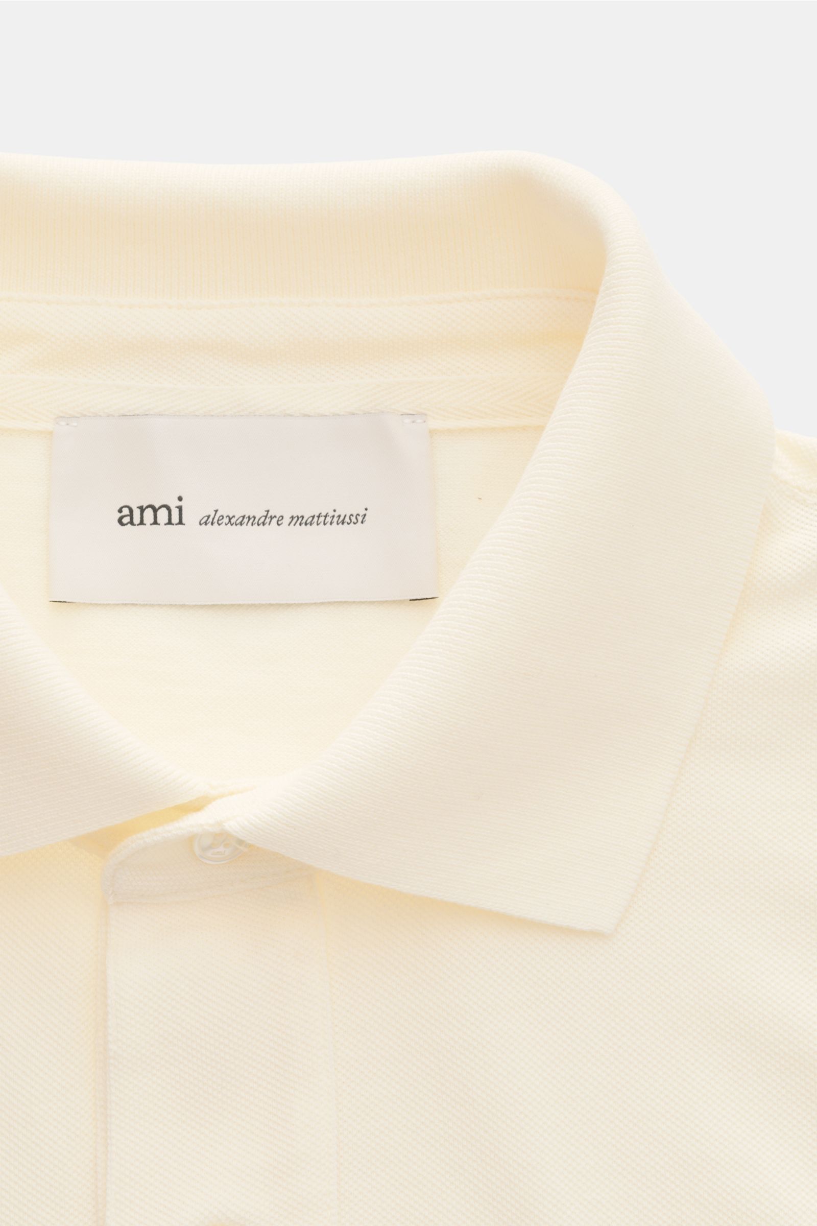 Close-up front view of Ami Paris Polo shirt cream showing signature collar, three-button placket, and textured piqué cotton fabric with logo stitching. 

Description: A casual classic among polo shirts: This piqué model in pure cotton with three-dimens