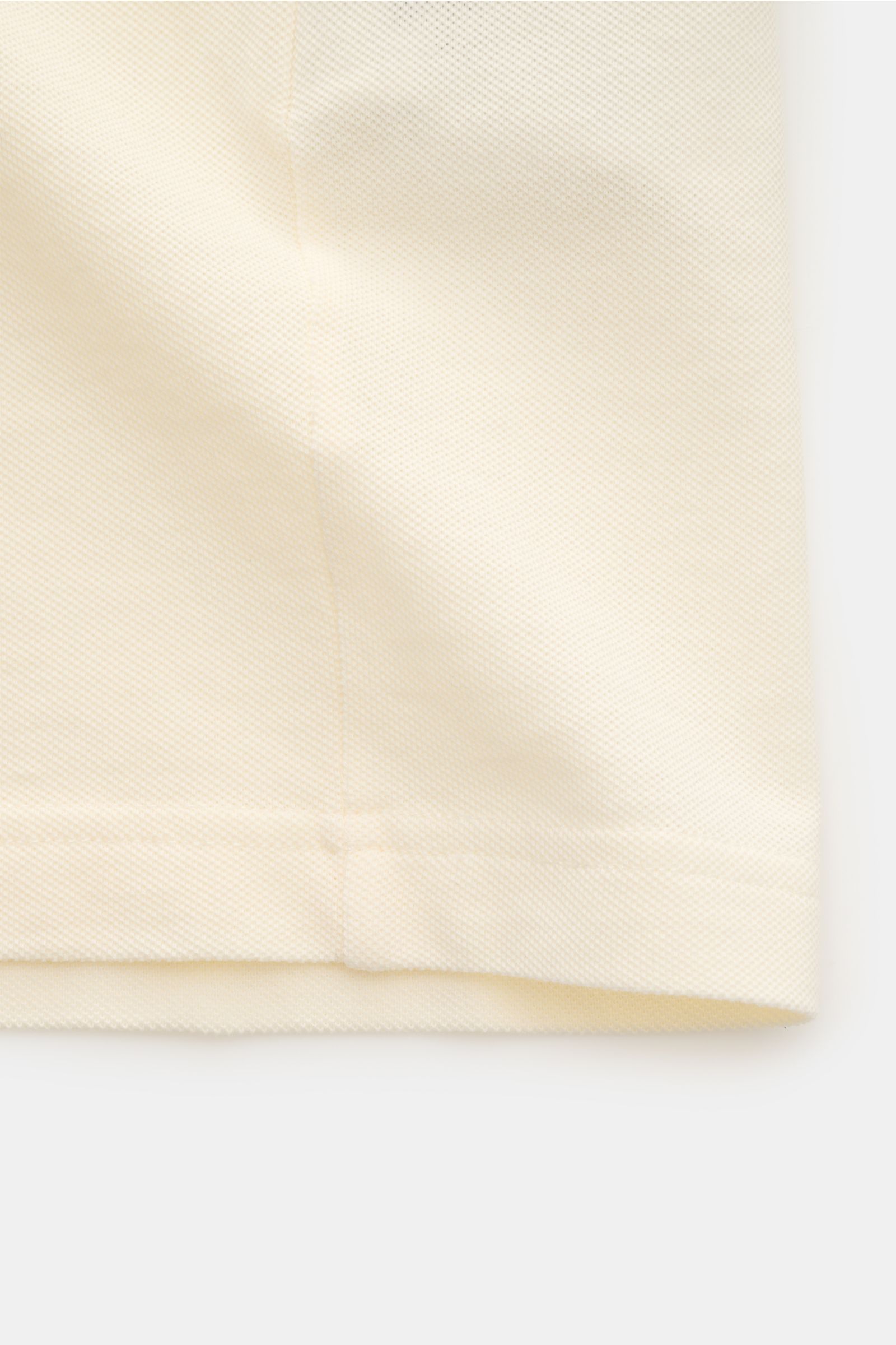 Close-up of the hem and textured piqué fabric of the Ami Paris Polo shirt cream, photographed from a side angle. A casual classic among polo shirts: This piqué model in pure cotton with three-dimensional ‘A’ stitching on the chest comes in a comfortable o