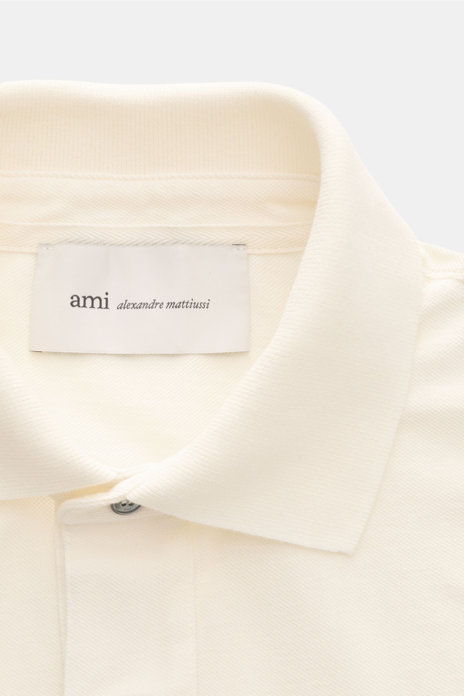Nahaufnahme des cremefarbenen Ami Paris Poloshirts 'Boxy Fit' mit typischem Polokragen, Drei-Knopf-Leiste und feiner Piqué-Struktur aus reiner Baumwolle.