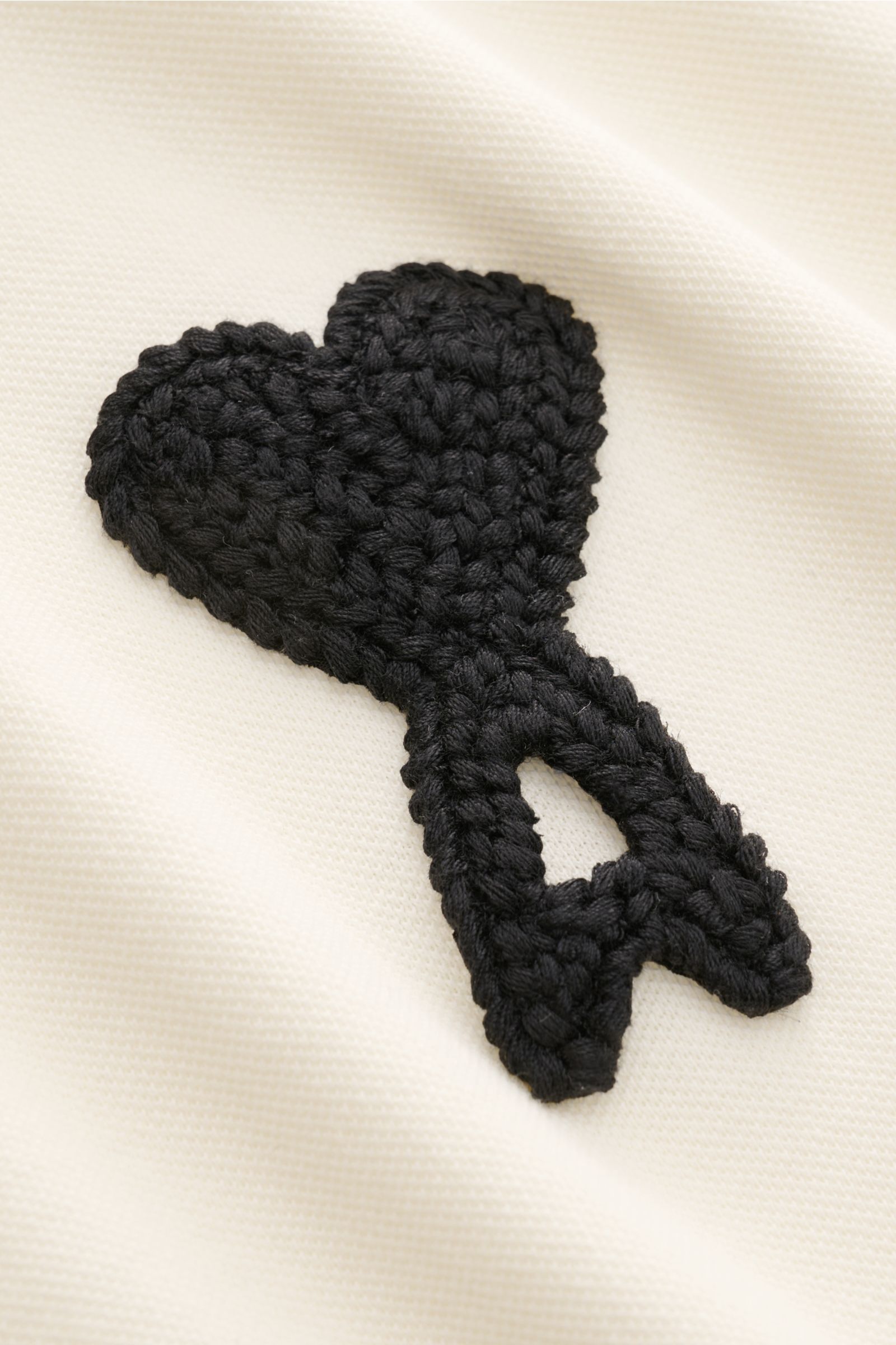 alt='Detailaufnahme des Ami Paris Poloshirts 'Boxy Fit' creme mit feiner Piqué-Struktur und labeltypischem schwarzen Logo-Stitching, fotografiert aus Nahperspektive. Klassiker in moderner Silhouette mit geradem Schnitt, reiner Baumwolle, weichem Griff, Ov