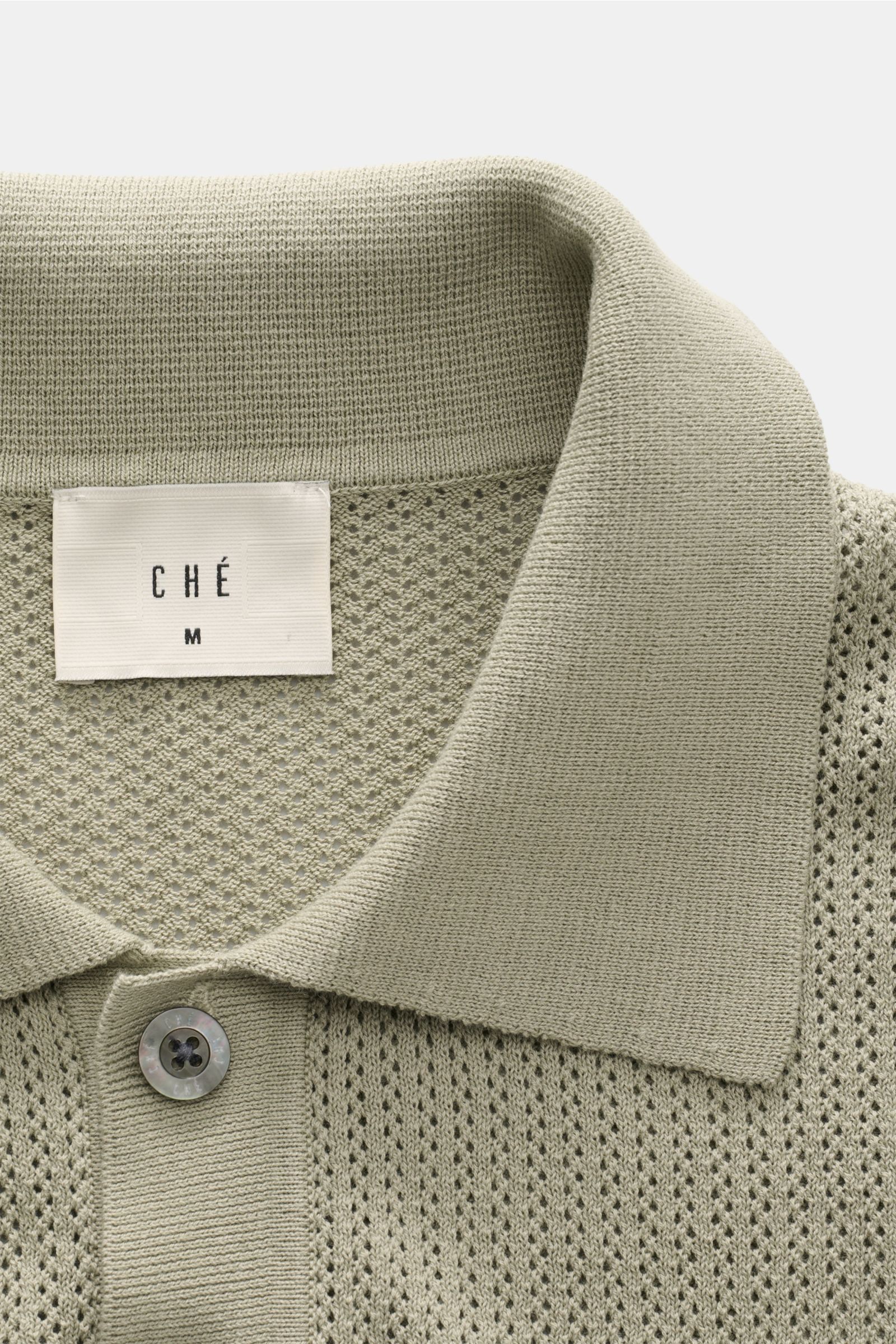 Nahaufnahme des Ché Kurzarm-Strickpolo 'Quinn' salbei von oben, luftiges Baumwoll-Strickmuster, Polokragen, Knopfleiste sichtbar.