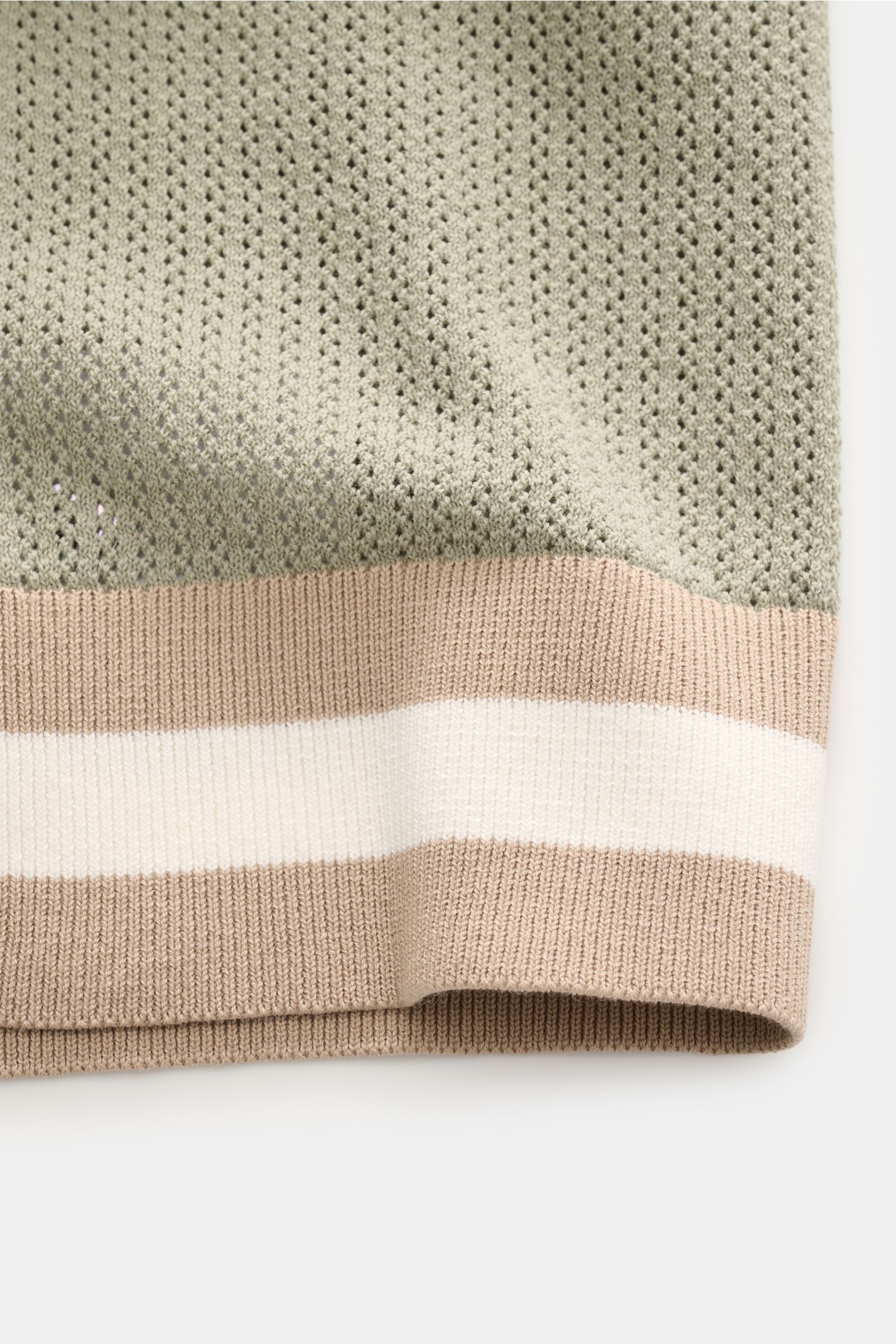 Nahaufnahme des luftigen Strickmusters und gestreifter Rippbündchen des Ché Kurzarm-Strickpolo 'Quinn' salbei, fotografiert von schräg oben.