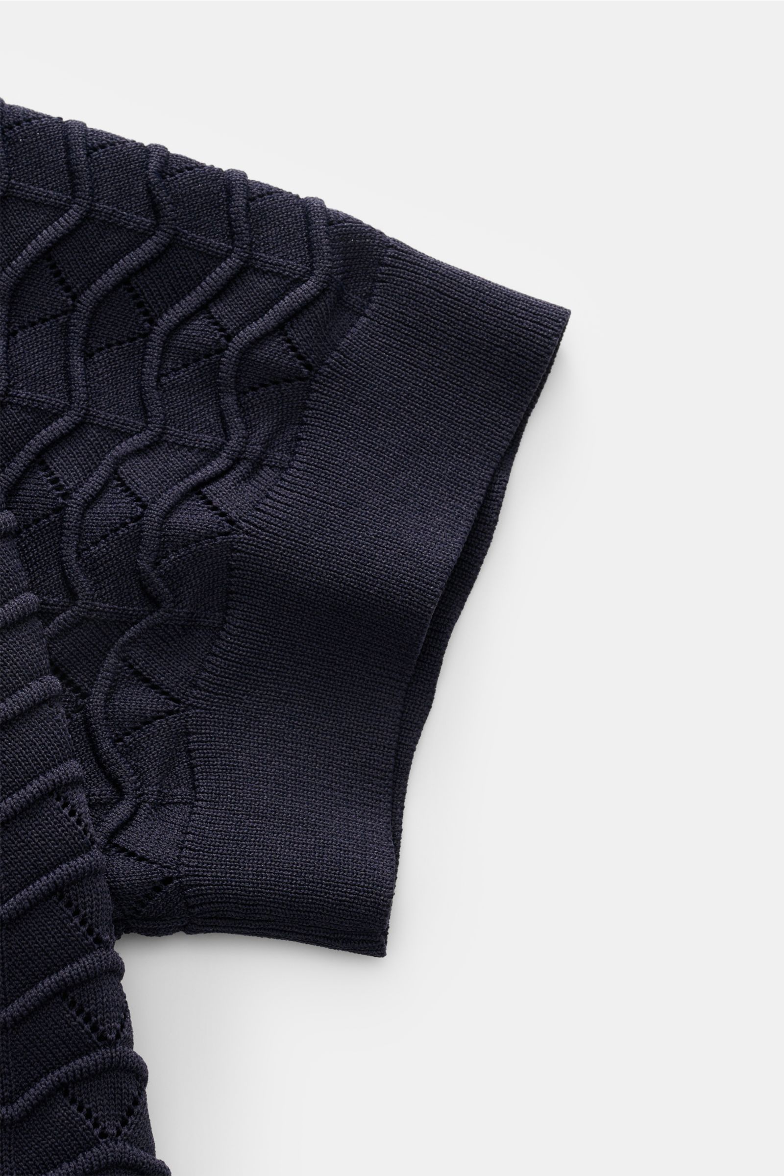 Close-up side view of the sleeve of the Ché Kurzarm-Strickpolo 'Ripple' navy, featuring a slim fit, airy structure knit. Lässige Beach Vibes: Das Strickpolo von CHÉ garantiert entspannte Looks für warme Tage.Mix aus Viskose und Microfaser