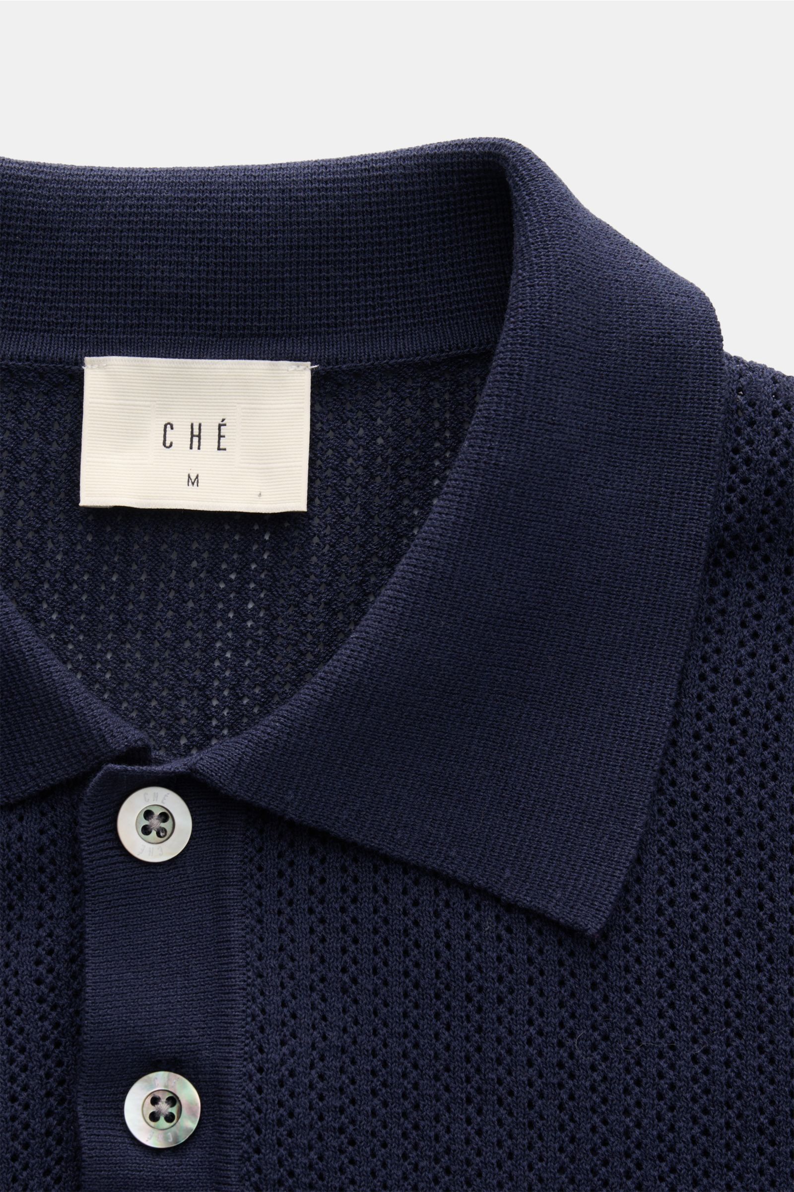 Close-up front view of Ché Kurzarm-Strickpolo 'Quinn' navy/hellbraun with a knitted collar, three-button placket, and airy cotton knit pattern.

Genießen Sie die Leichtigkeit des Sommers mit dem luftigen Kurzarm-Strickpolo 'Quinn' von CHÉ. Kontrastiere