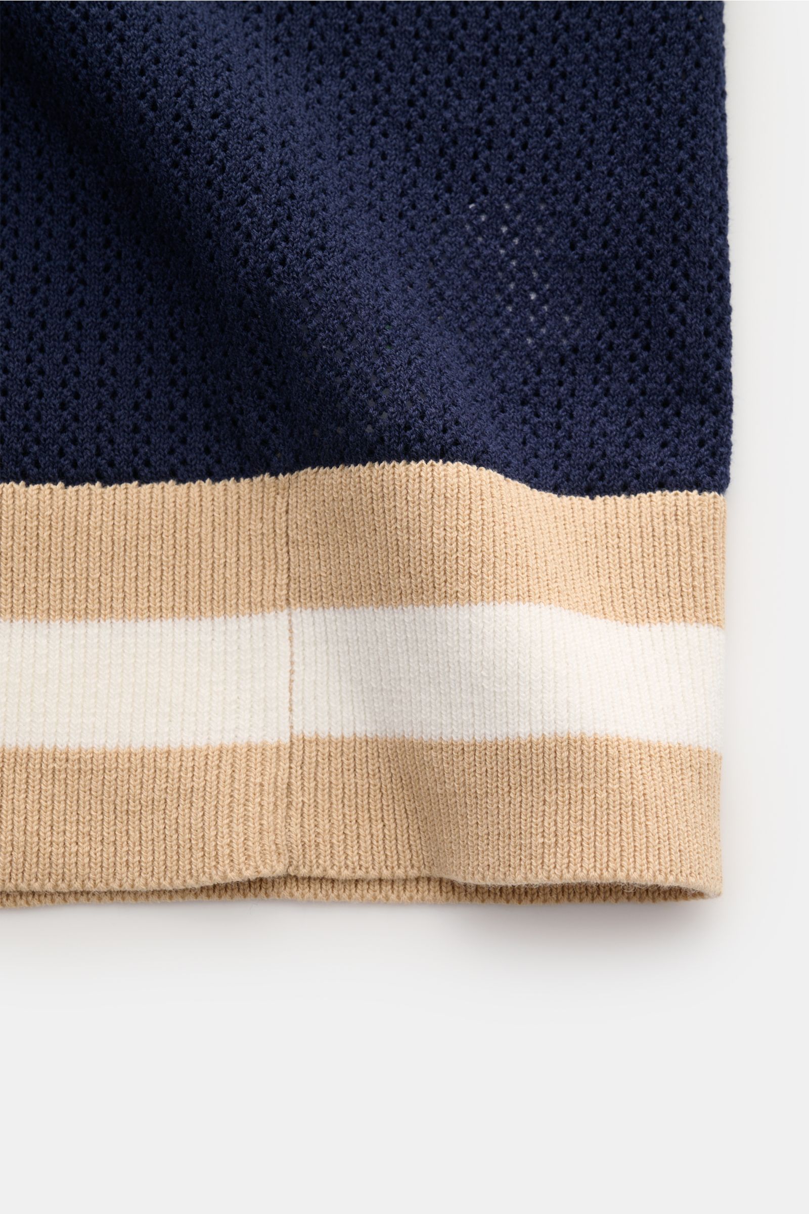 Close-up front view of the hem of the Ché Kurzarm-Strickpolo 'Quinn' navy/hellbraun, showing the airy knit pattern and striped ribbed cuffs. Genießen Sie die Leichtigkeit des Sommers mit dem luftigen Kurzarm-Strickpolo 'Quinn' von CHÉ. Kontrastierende,