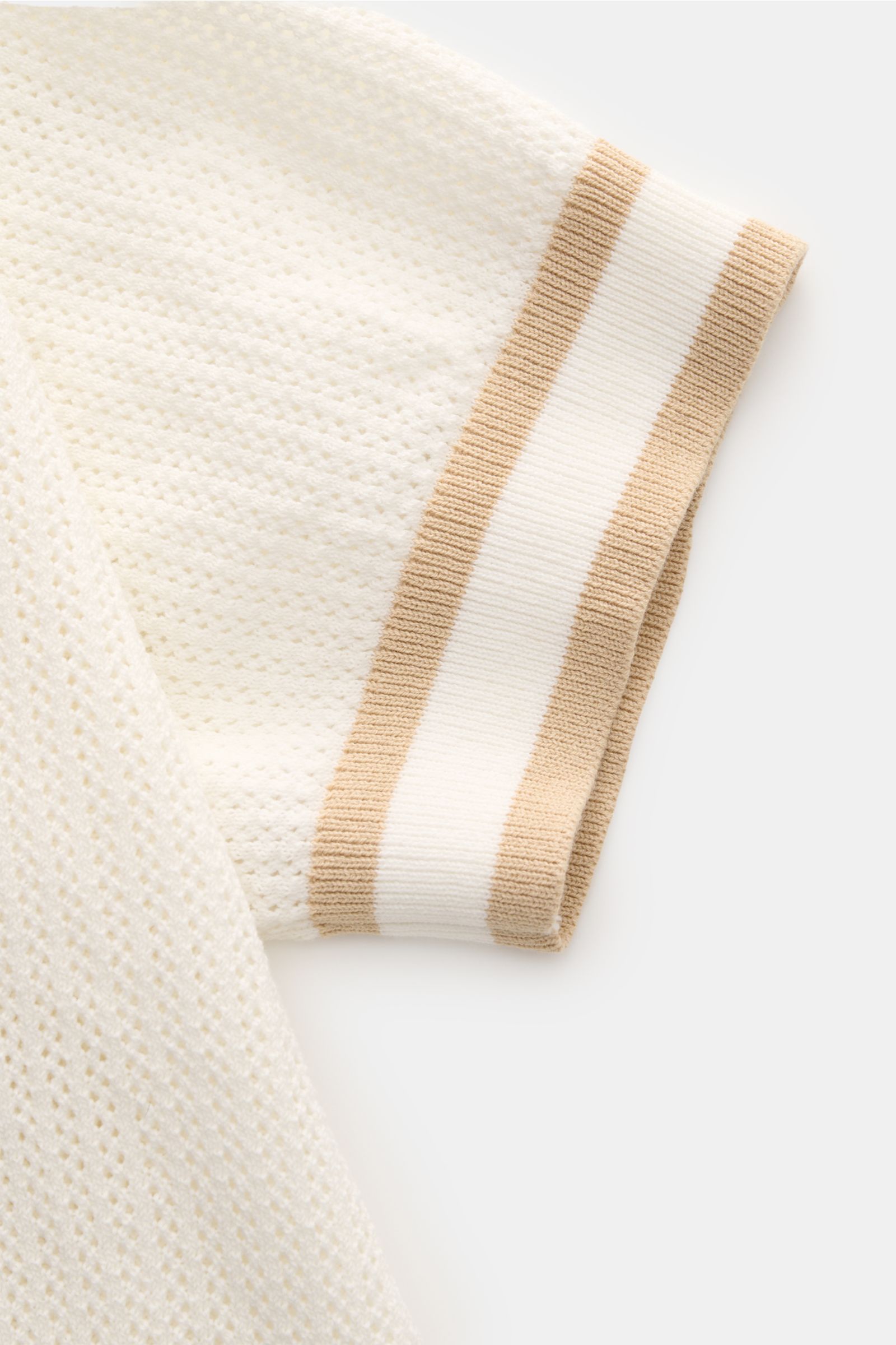 Close-up of the sleeve of Ché Kurzarm-Strickpolo 'Quinn' weiß/hellbraun, photographed from above, showing the airy knit pattern and contrasting striped ribbed cuff. Genießen Sie die Leichtigkeit des Sommers mit dem luftigen Kurzarm-Strickpolo 'Quinn' von 