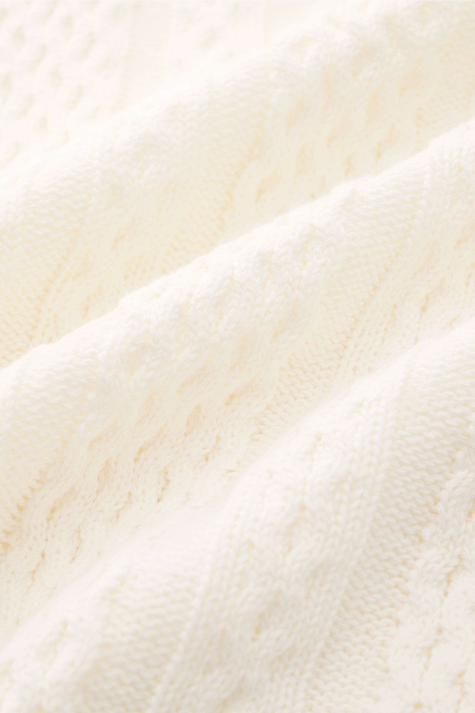 Close-up of the Ché Kurzarm-Strickpolo 'Santino' creme showing its coarse asymmetric knit pattern and texture, photographed from a top angle. Strickkunst mit Twist: Das 'Santino' Kurzarm-Poloshirt von CHÉ überzeugt mit einem groben Muster mit asymmetrisch