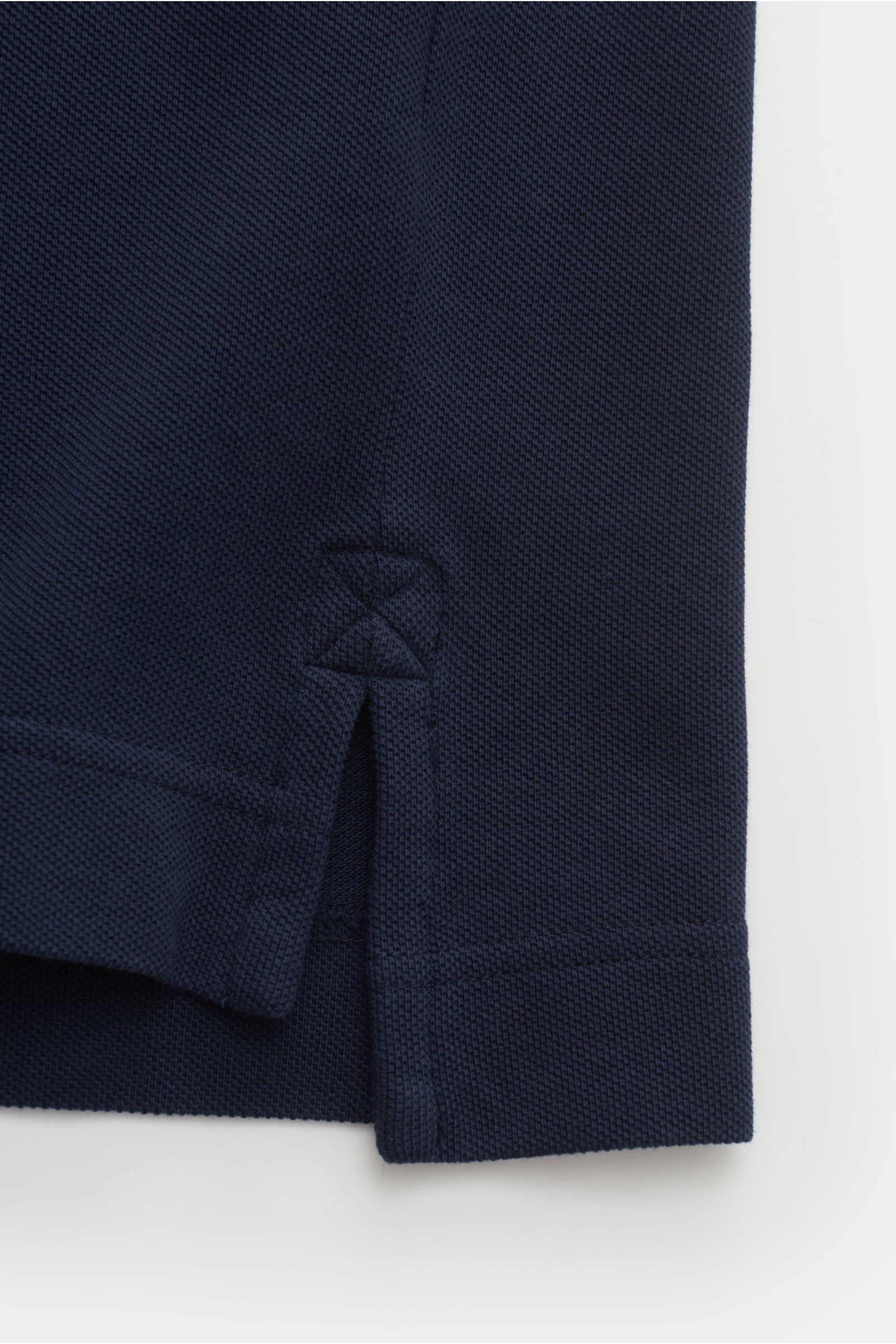 Close-up image of the side hem and slit of the Canada Goose Poloshirt 'Beckley' navy, showcasing the pure cotton piqué fabric, structured texture, garment-dyed finish, and detailed stitching. Photograph taken from a flat-lay side perspective. Das klass