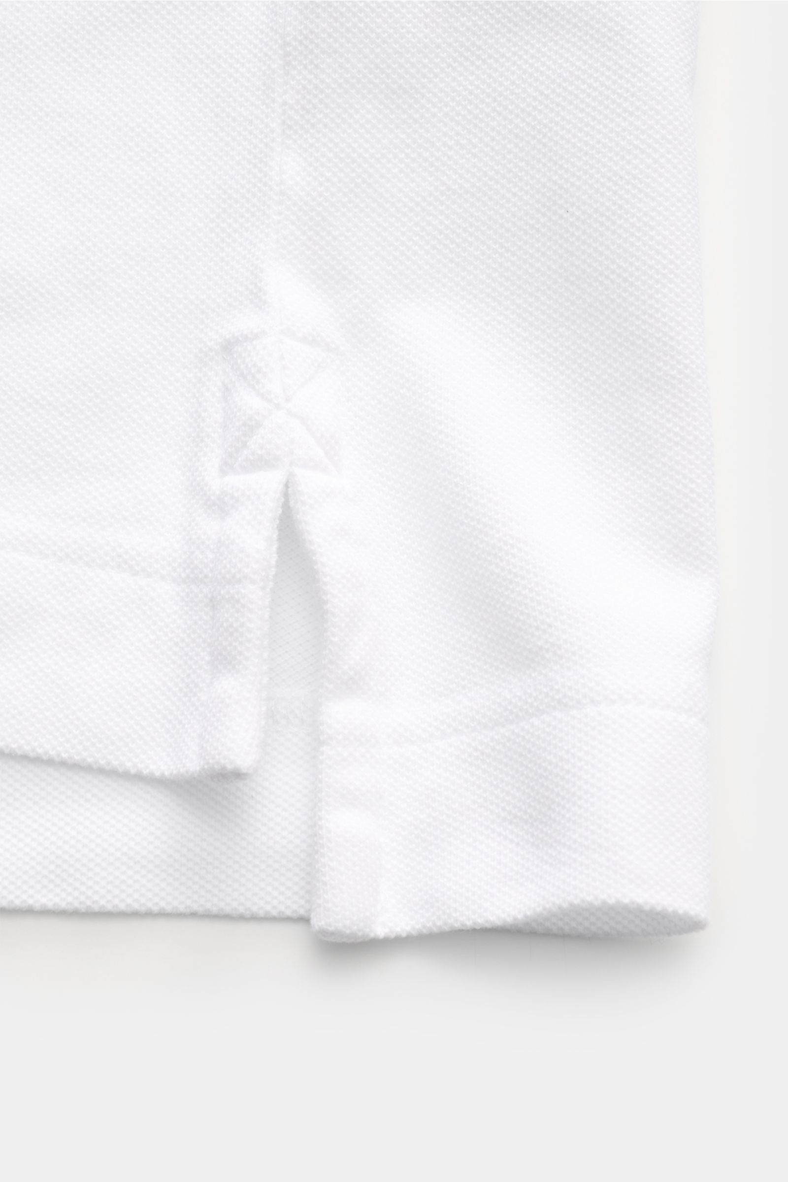 Close-up of the side hem with slit of the Canada Goose Poloshirt 'Beckley' weiß, showing textured cotton piqué fabric from a front-side perspective. The classic polo shirt 'Beckley' is a must-have in the sporty men's wardrobe: made from pure cotton piqué,