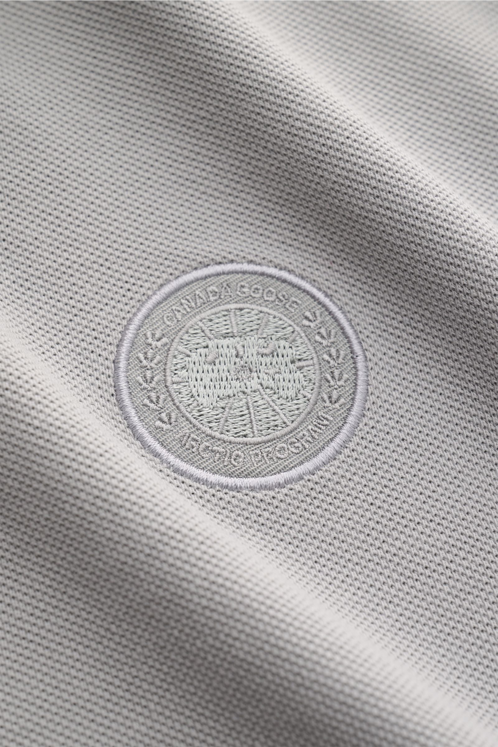 Close-up front view of the Canada Goose Poloshirt 'Beckley' grau showing the textured pure cotton piqué fabric with garment-dyed finish and the embroidered CANADA GOOSE patch on the chest. Das klassische Poloshirt ist ein Must-have in der sportiven Her
