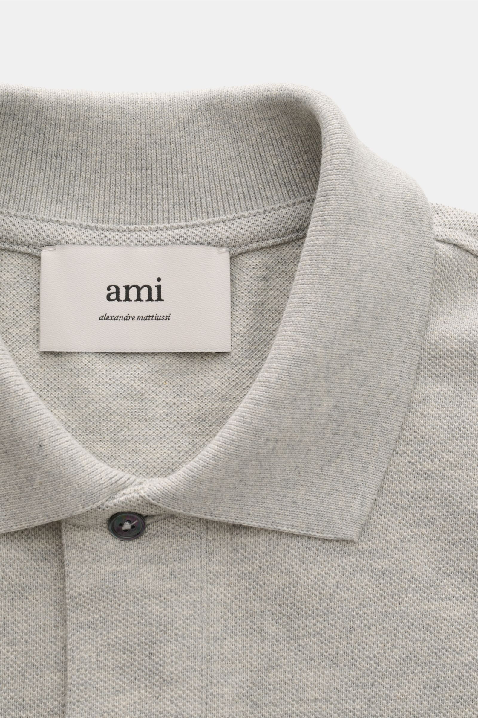 A close-up front view of the Ami Paris Poloshirt grau meliert showing the grey melange fabric, typical polo collar, and one visible button. Ein schöner Klassiker unter den Poloshirts: Das ikonisches Piqué-Modell aus reiner Bio-Baumwolle mit dem 'A'-Sti