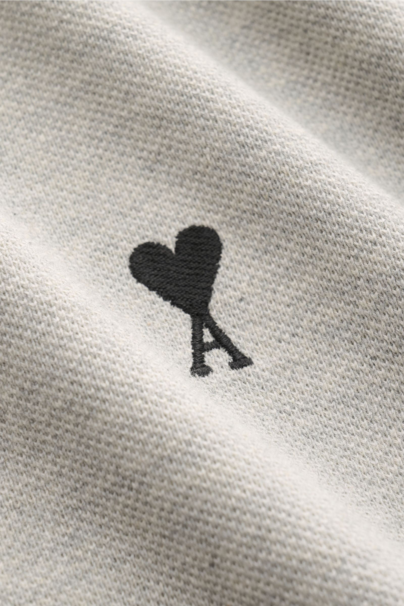 Close-up front view of the Ami Paris Poloshirt grau meliert showing the black heart-shaped 'A' stitching on soft grey melange piqué fabric, made from organic cotton. 

Description:  
Ein schöner Klassiker unter den Poloshirts: Das ikonisches Piqué-Mode