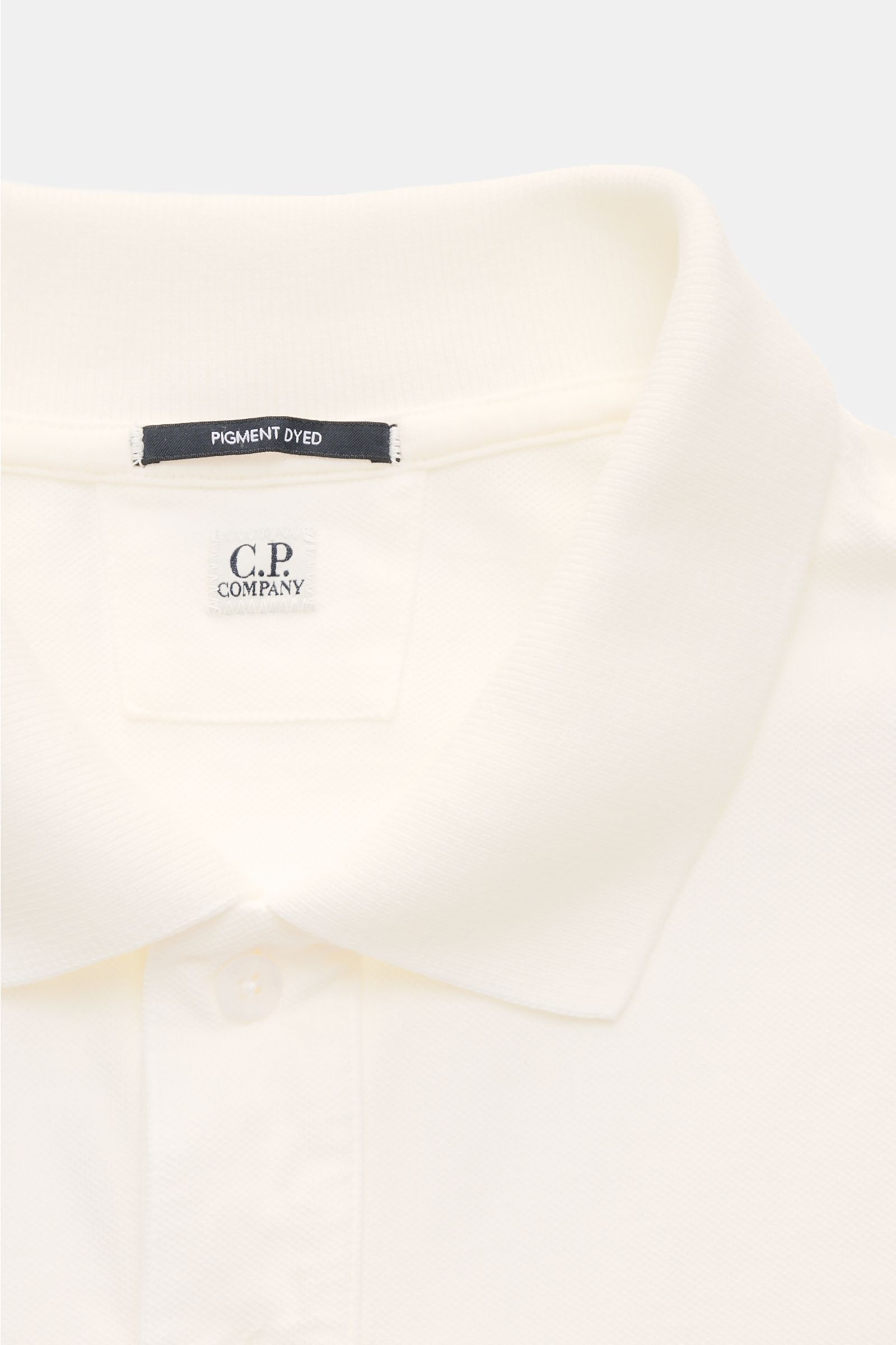 C.P. Company Poloshirt weiß aus Baumwoll-Piqué, Slim Fit, klassischer Kragen, Knopfleiste, Weblabel, elastische Ärmelbündchen, Detailaufnahme von oben.