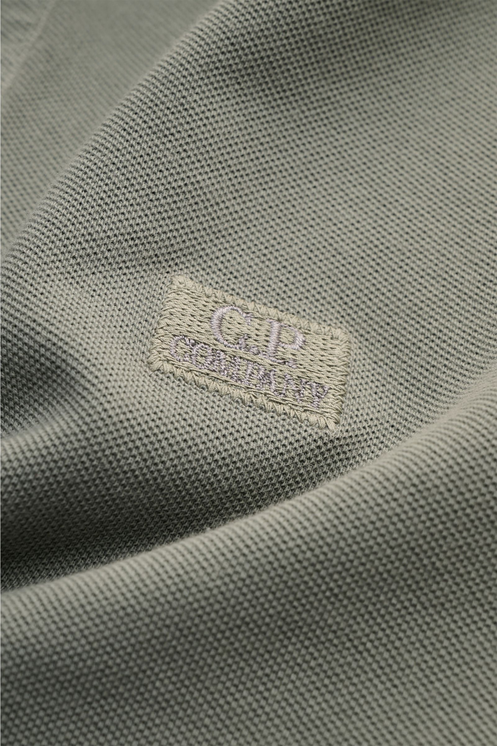 Nahaufnahme des grauen C.P. Company Poloshirts aus Baumwoll-Piqué mit feinem Stitching des Logos auf der Brust, weiche Struktur sichtbar.