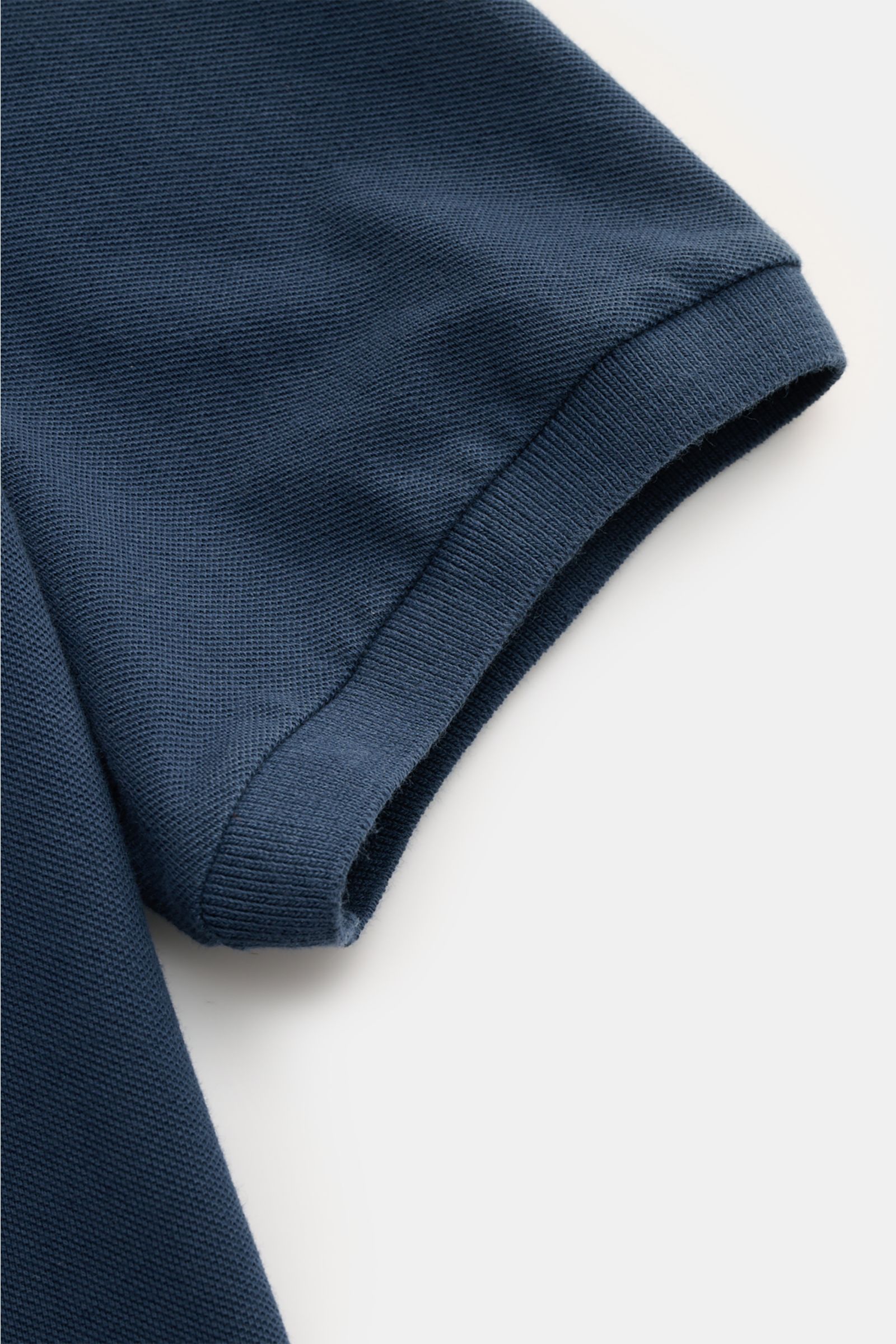 Nahaufnahme des C.P. Company Poloshirts dunkelblau, kurzärmelig, aus weichem Baumwoll-Piqué mit elastischem Ärmelbündchen, fotografiert von oben.