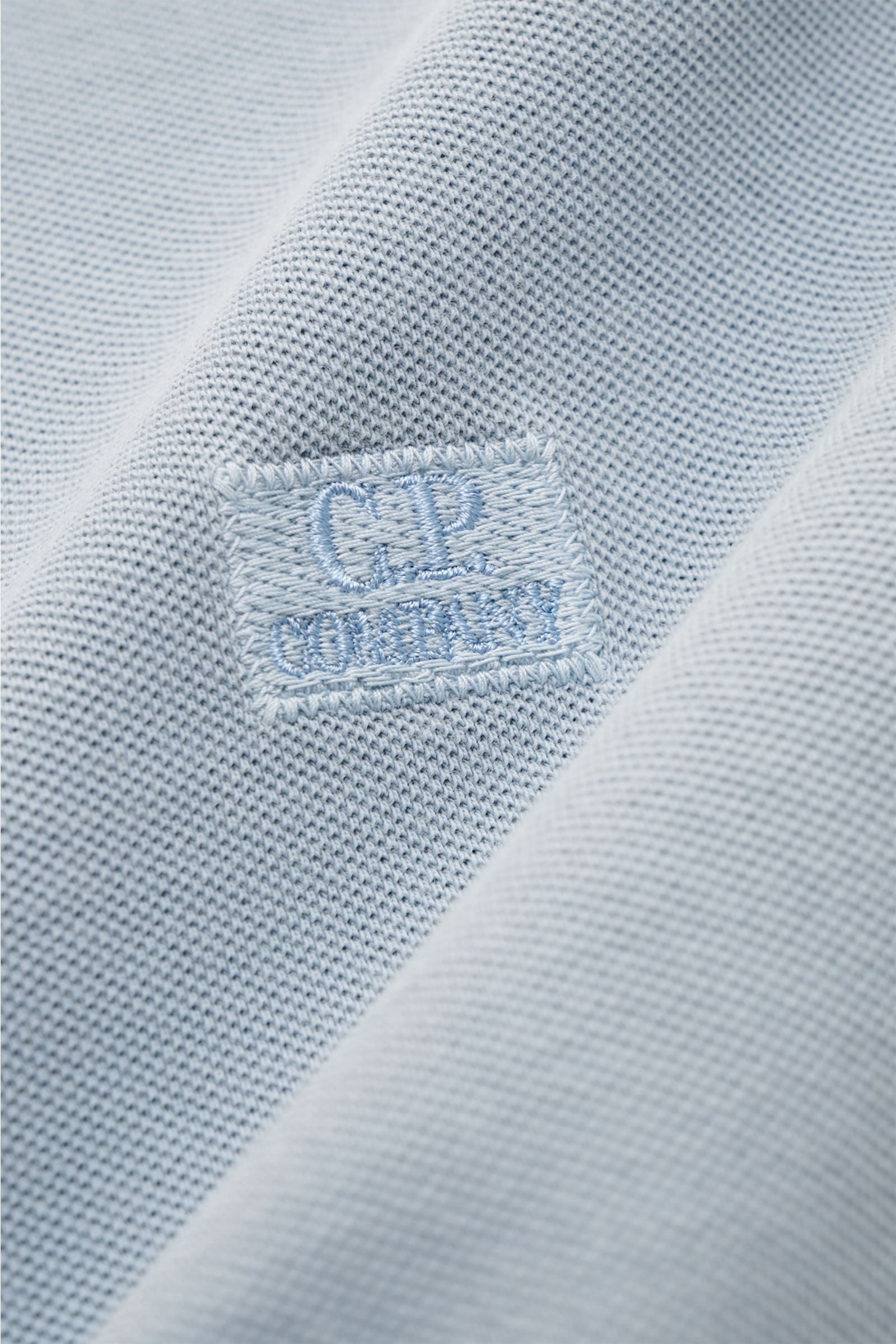 Nahaufnahme des C.P. Company Poloshirts rauchblau aus reinem Baumwoll-Piqué mit feinem Stitching und Weblabel, leicht strukturierte Oberfläche.