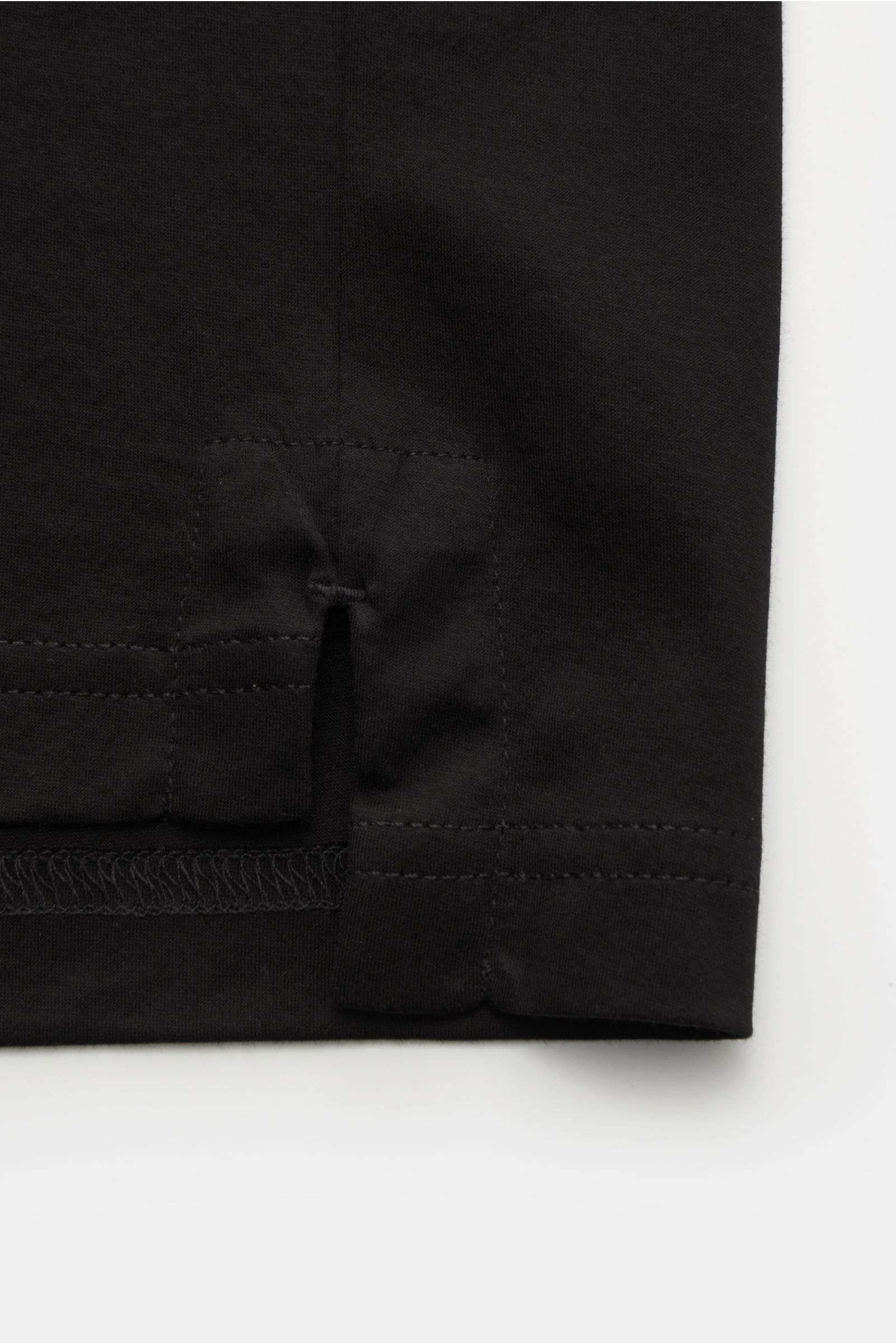 Close-up of the lower side seam and short hem slit of the Stefan Brandt Jersey-Poloshirt 'Luca' schwarz, photographed from a front side perspective. The exclusive jersey polo shirt features high-quality organic Pima cotton with a particularly soft touch a