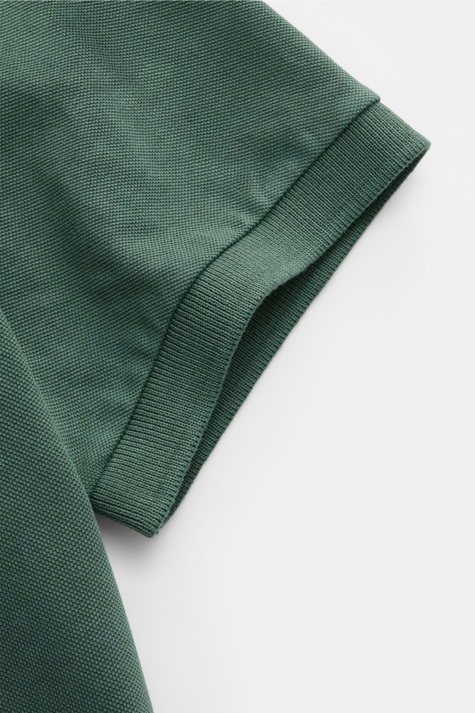 Nahaufnahme des dunkelgrünen Della Ciana Poloshirts, perspektivisch auf das elastische Ärmelbündchen und die feine Baumwoll-Piqué-Struktur fokussiert.