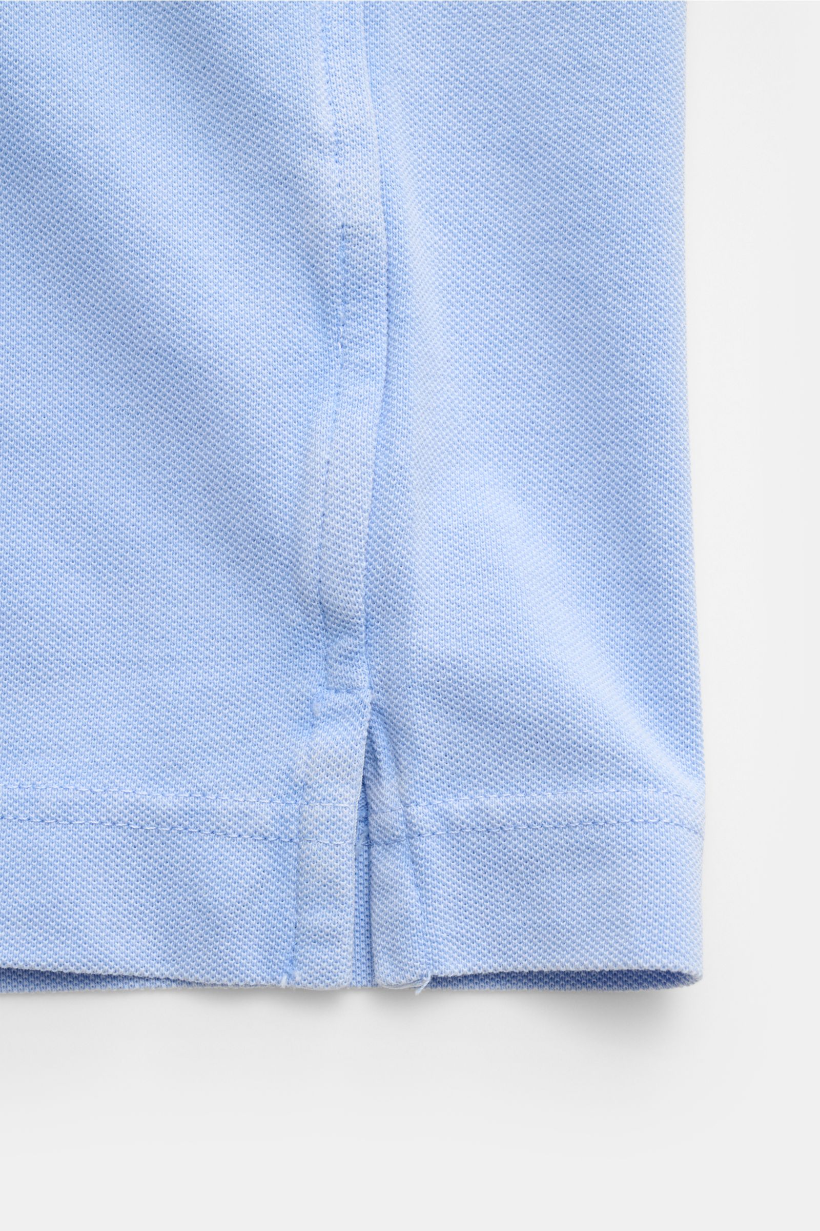 Nahaufnahme des seitlichen Saums mit Saumschlitzen des hellblauen Della Ciana Poloshirts, stückgefärbt aus reiner Baumwolle mit feiner Piqué-Struktur.