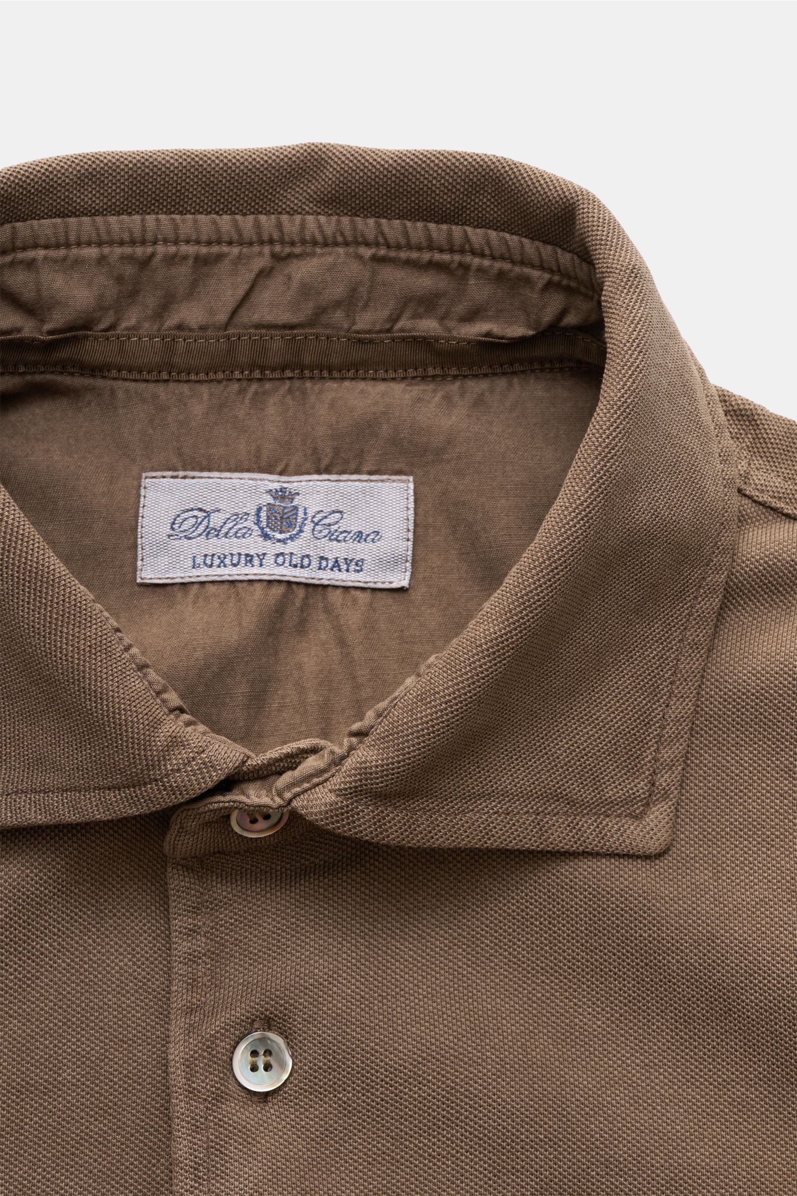 Nahaufnahme des Della Ciana Poloshirts braun von oben, zeigt Baumwoll-Piqué, Polokragen, Drei-Knopf-Leiste, feine Struktur.