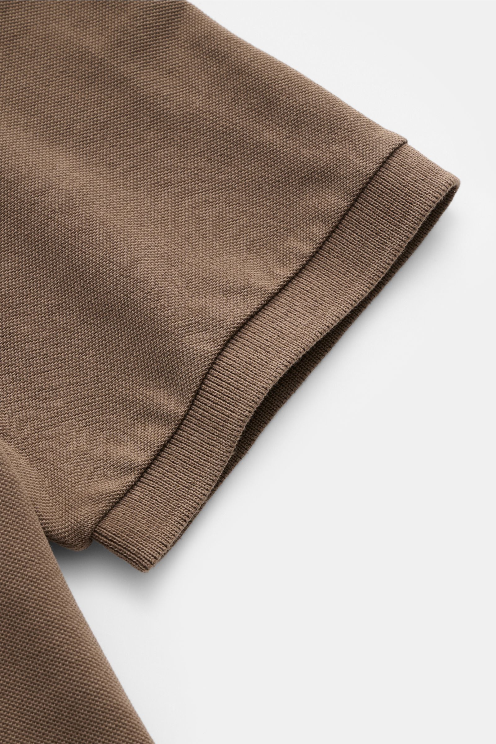 Nahaufnahme des Ärmels vom braunen Della Ciana Poloshirt, stückgefärbt, reine Baumwolle, feine Piqué-Struktur, elastisches Bündchen, fotografiert von oben.