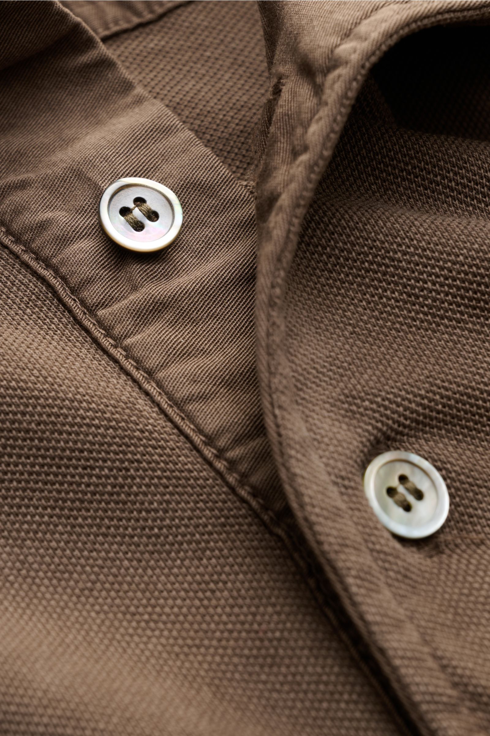 Nahaufnahme des braunen Della Ciana Poloshirt braun mit feiner Piqué-Struktur, Knöpfen und Polokragen, seitlich fotografiert.