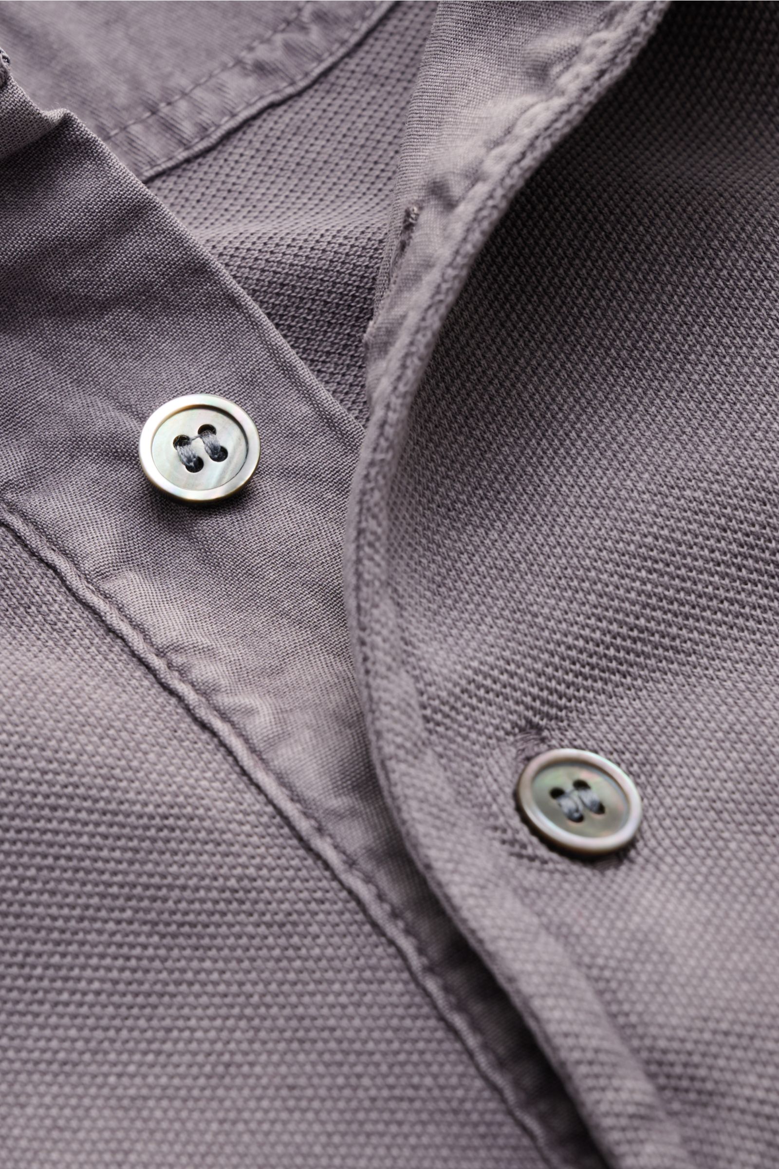 Nahaufnahme aus schräger Perspektive des Della Ciana Poloshirt grau, stückgefärbt aus reiner Baumwolle mit feiner Piqué-Struktur, Polokragen, Drei-Knopf-Leiste und elastischen Ärmelbündchen.