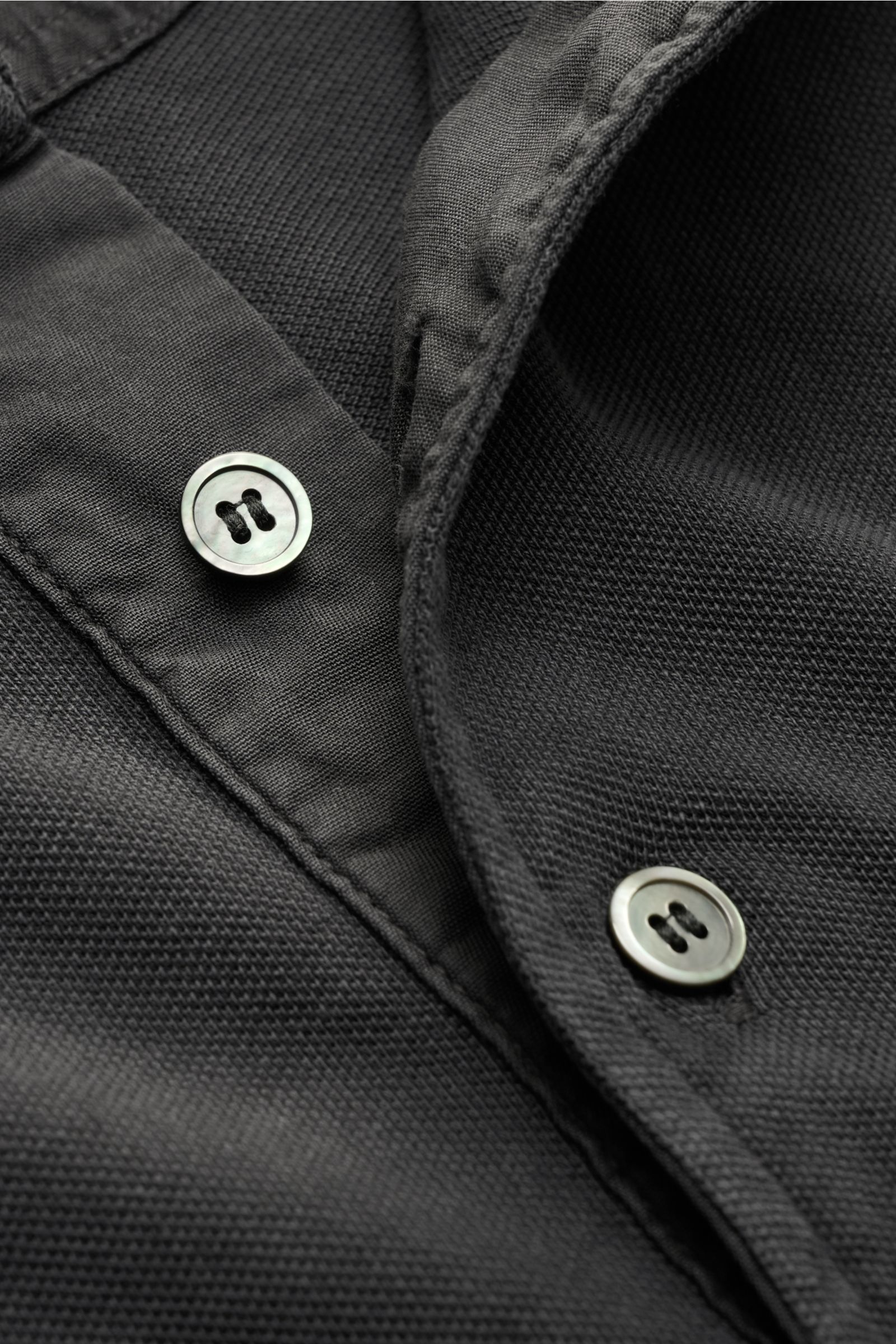 Nahaufnahme von Della Ciana Poloshirt dunkelgrau, perspektivisch auf den Kragen mit typischer Drei-Knopf-Leiste, feiner Piqué-Struktur, reine Baumwolle, garment dyed, Regular Fit, elastische Ärmelbündchen sichtbar.