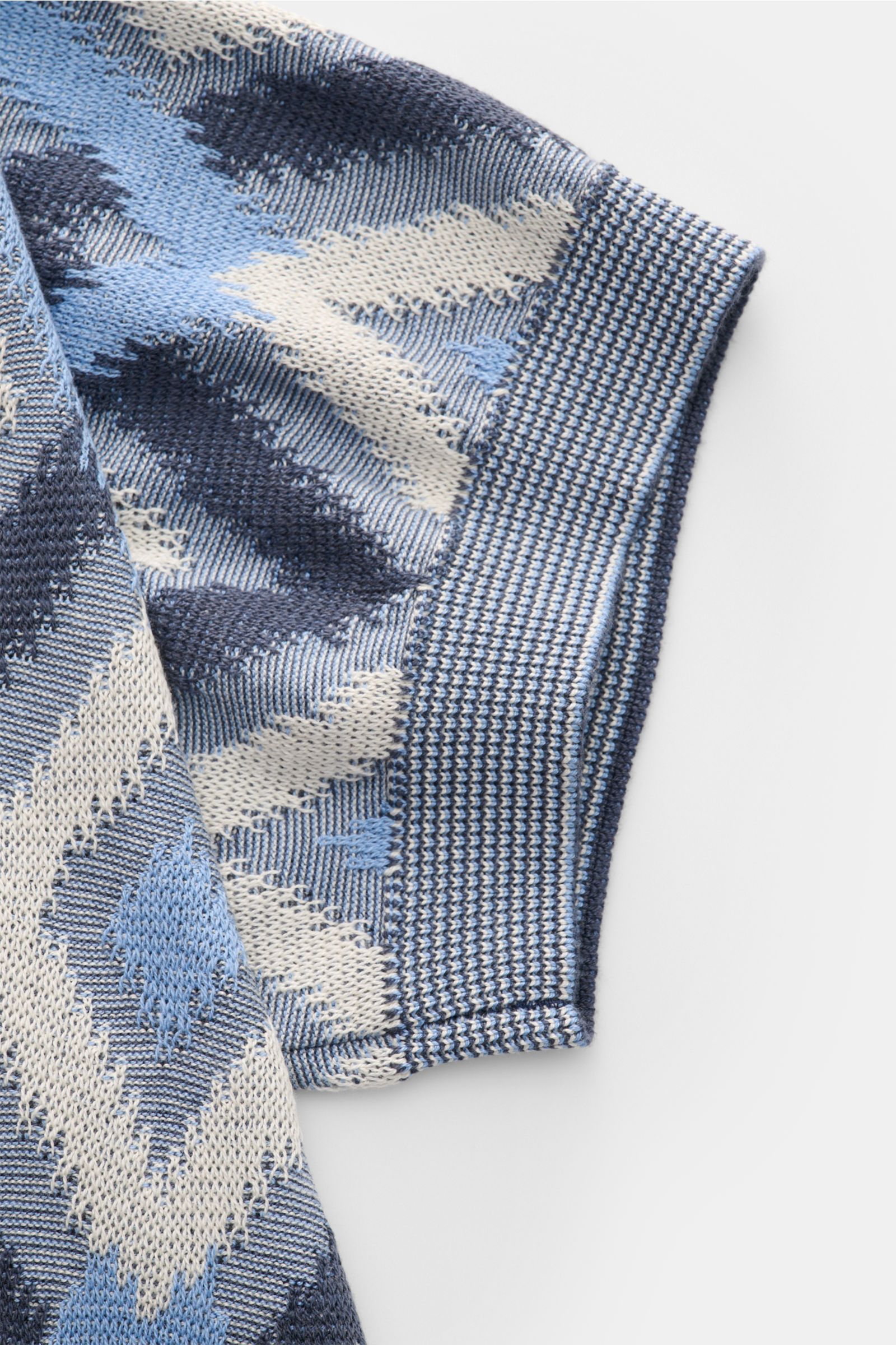 Close-up side view of the sleeve of the Piacenza 1733 Kurzarm-Strickpolo rauchblau/blau/creme gemustert, featuring a lightweight silk and cotton knit with airy texture and contrast diamond pattern.

Ein Hauch von Luxus: Dieses Kurzarm-Strickpolo von PI