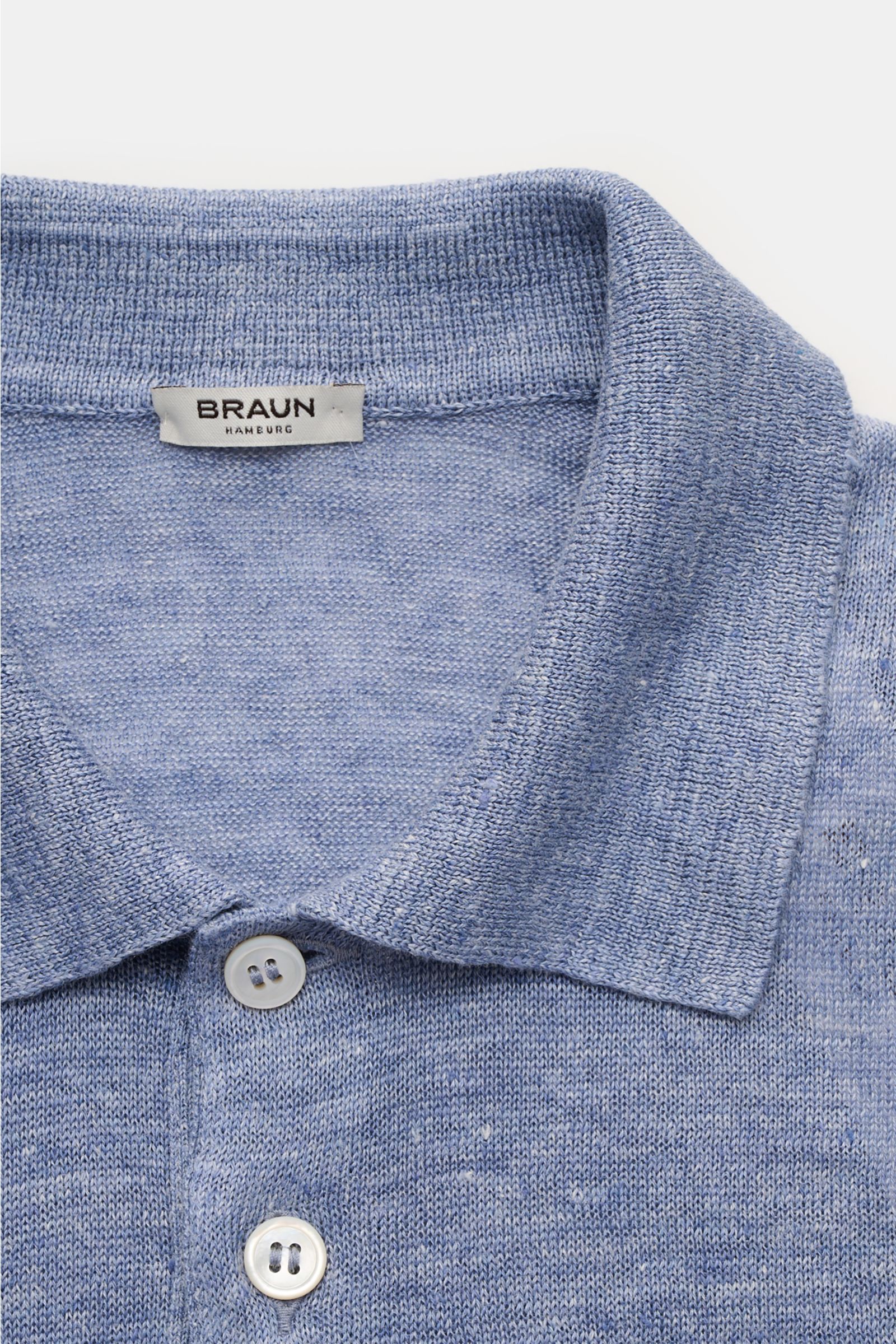 Nahaufnahme eines BRAUN Hamburg Leinen Kurzarm-Strickpolo hellblau von oben, zeigt Polokragen, Drei-Knopf-Leiste, feines Strickbild und materialtypische Leinenstruktur.