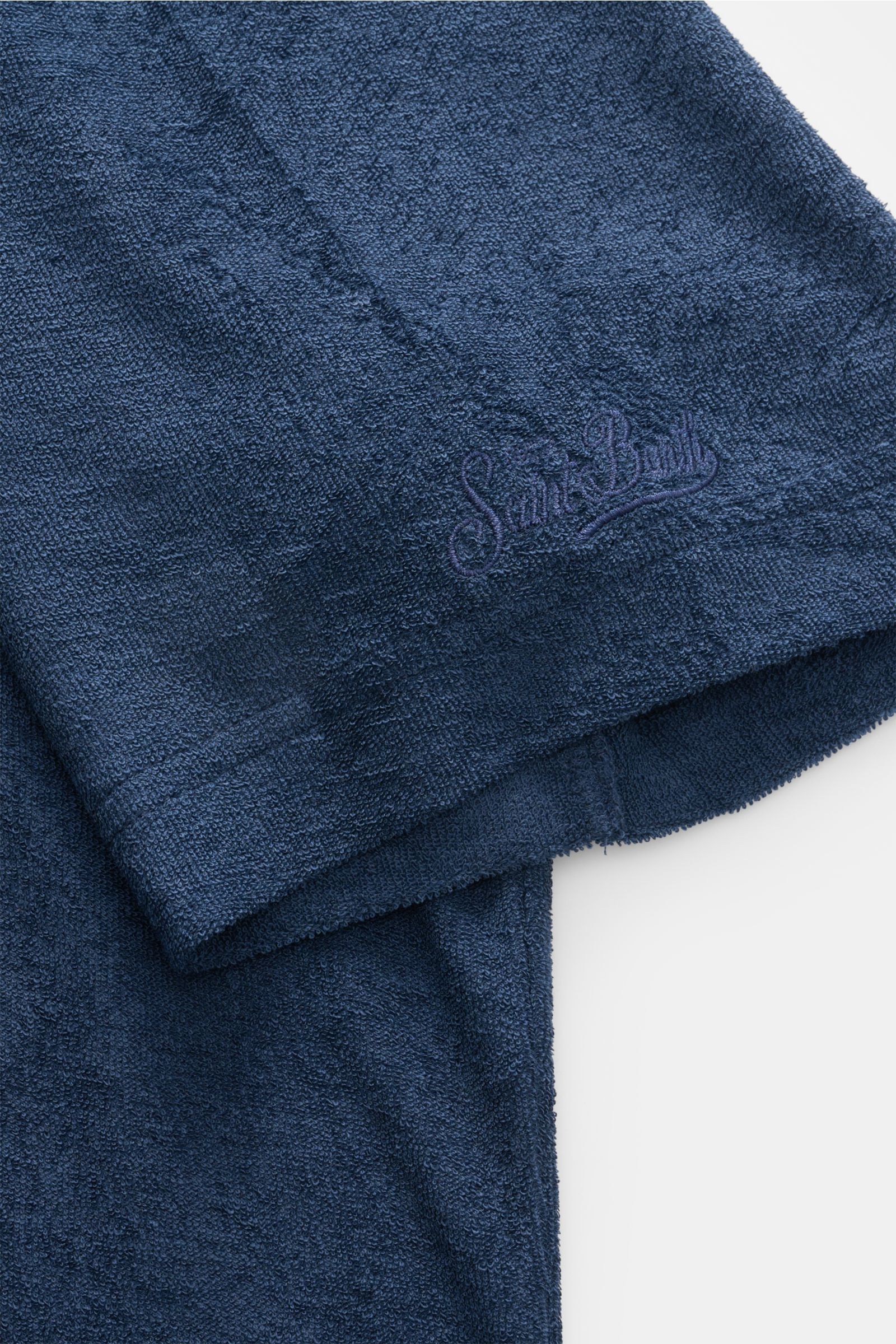 Nahaufnahme des MC2 Saint Barth Frottee-Poloshirt 'Jeremy' navy Ärmel mit Logo-Stitching, weichem Lyocell-Baumwollstoff, Slim Fit, offener Kragenleiste und kurzen Saumschlitzen, fotografiert von schräg oben.