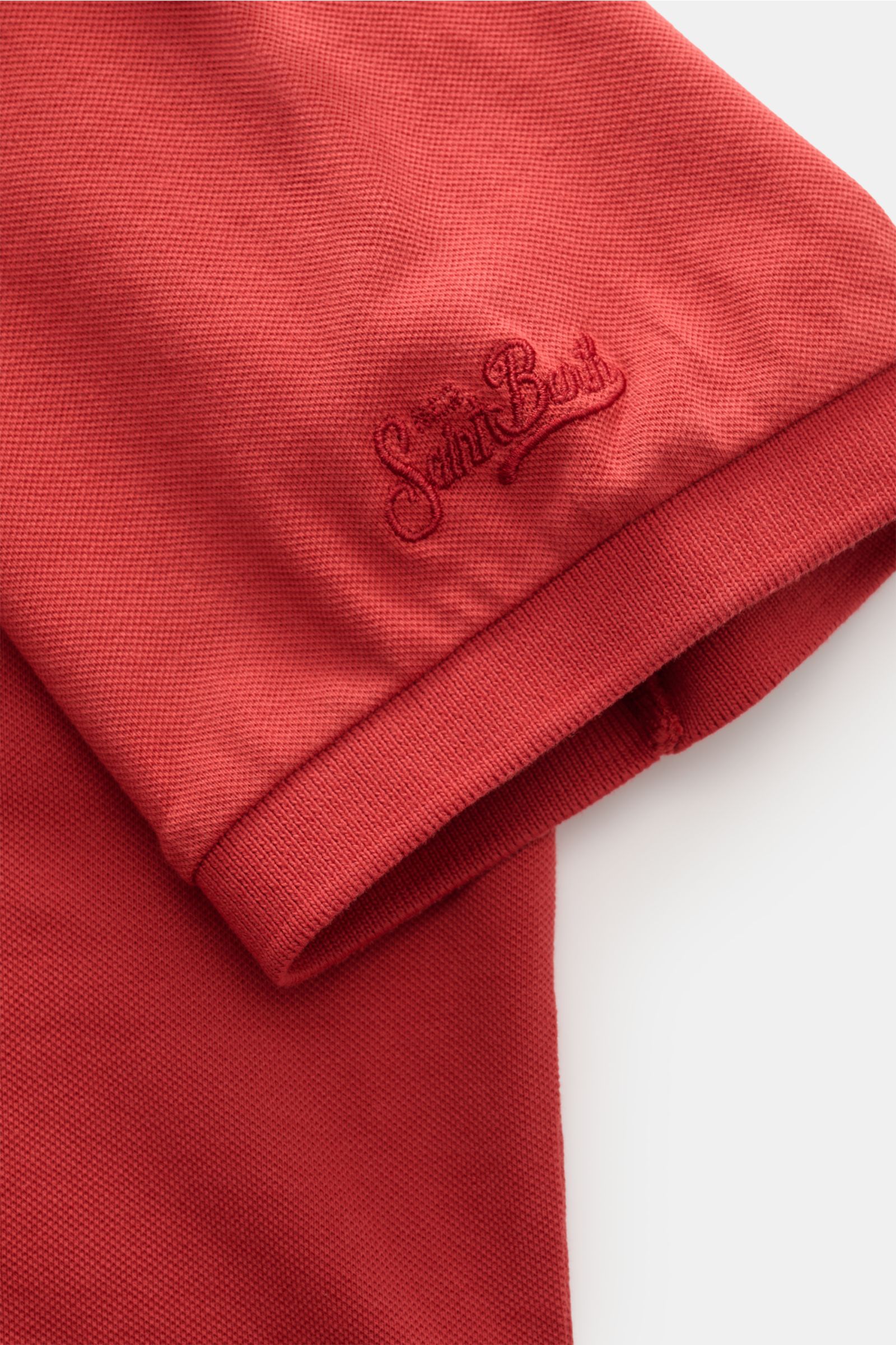 MC2 Saint Barth Poloshirt 'Charles' rot shown from a close-up side angle, highlighting the elastic cotton piqué fabric, soft texture, logo stitching on the sleeve, comfortable ribbed cuffs, and short hem slits. 