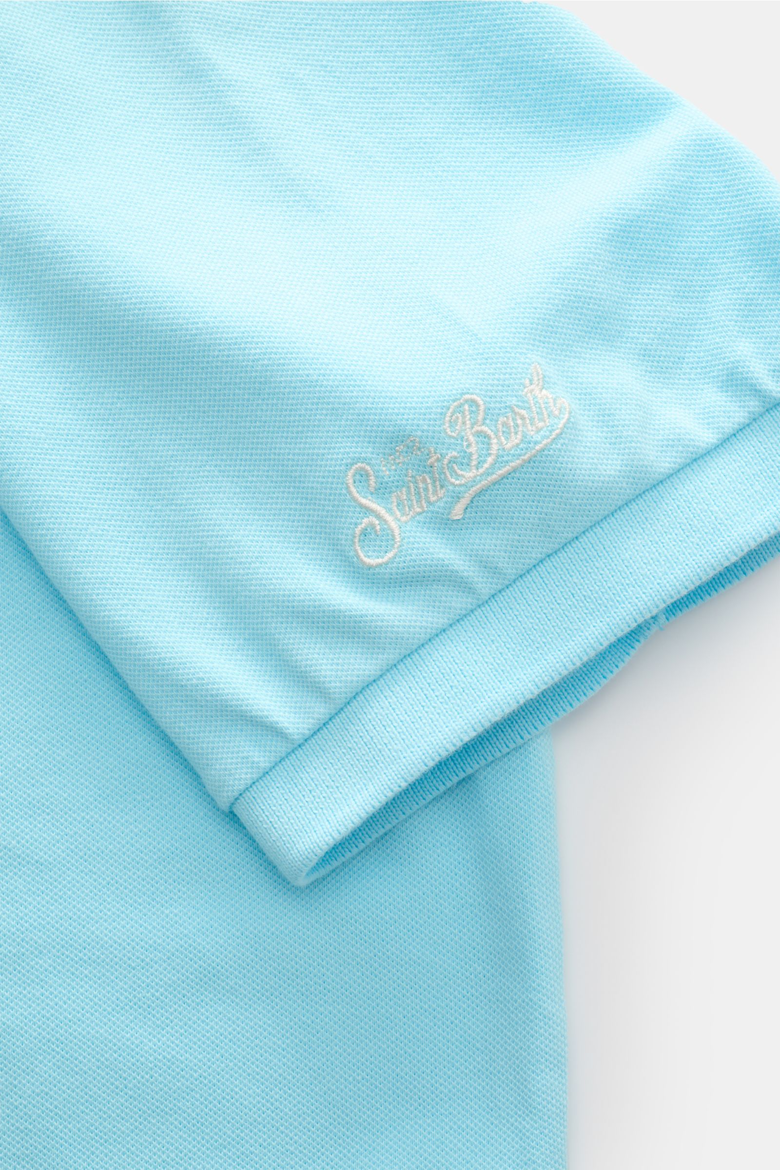 Close-up side view of the sleeve hem and logo stitching of the MC2 Saint Barth Poloshirt 'Charles' türkis in elastic, soft cotton piqué fabric, featuring ribbed cuffs and short side slits. 