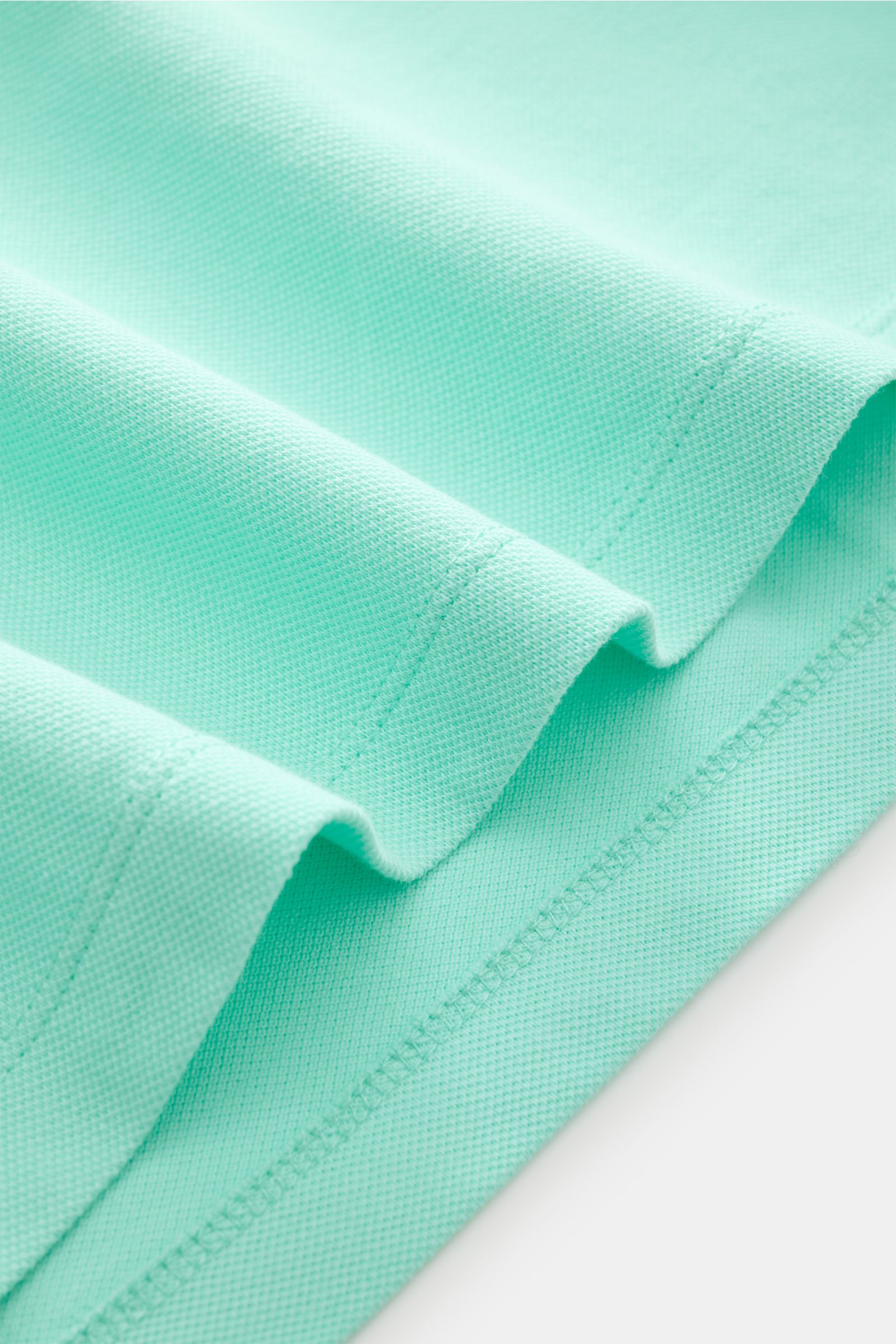 Close-up image of the fabric texture of the MC2 Saint Barth Poloshirt 'Charles' mintgrün, photographed from a top-down angle, showing mint green elastic cotton piqué with a soft feel, detailed stitching, and folded edges. 