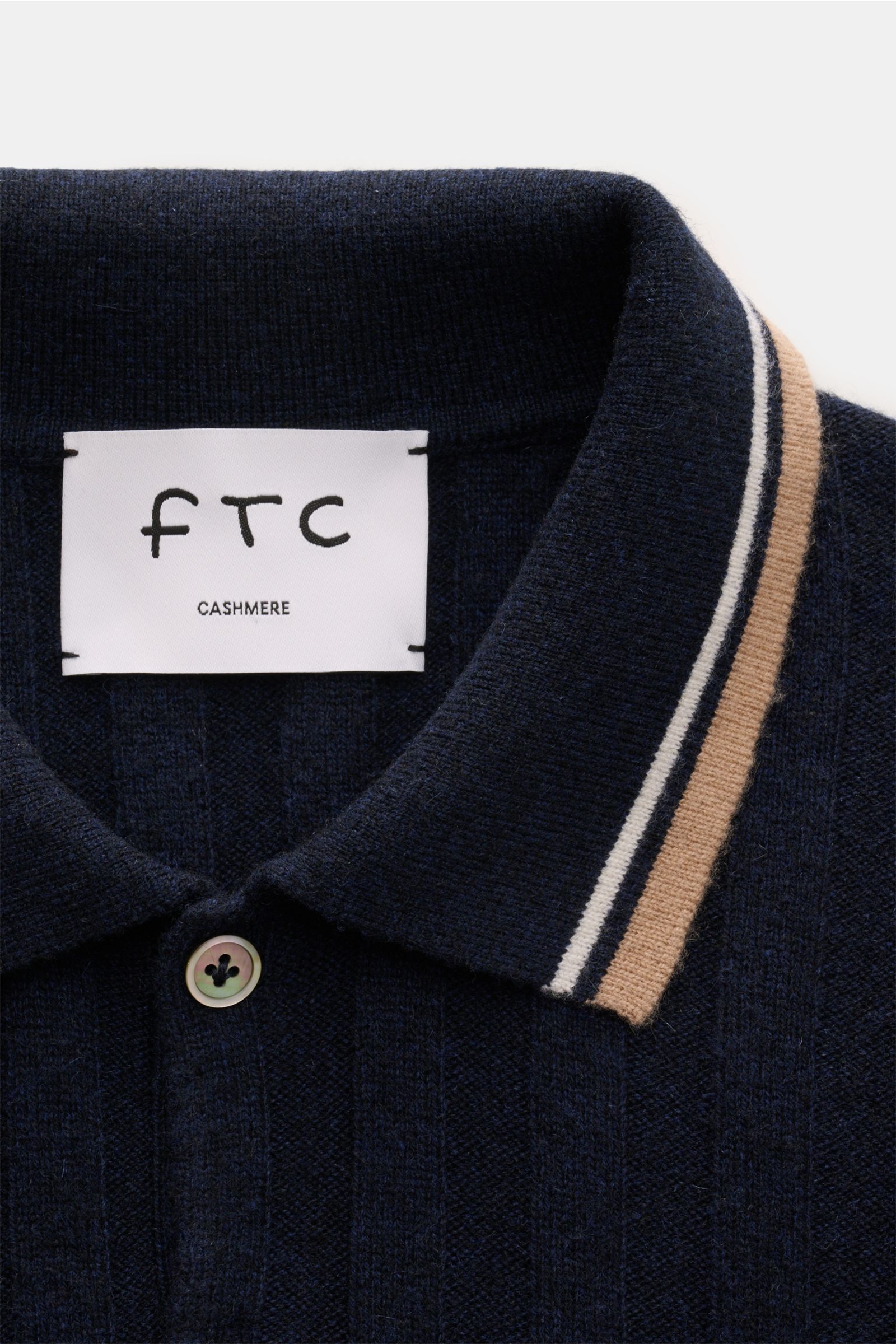 Nahaufnahme des FTC Cashmere Kurzarm-Strickpolo navy von oben, breites Rippstrick-Design, zwei Knöpfe, Kontraststreifen am Kragen und Bündchen.
