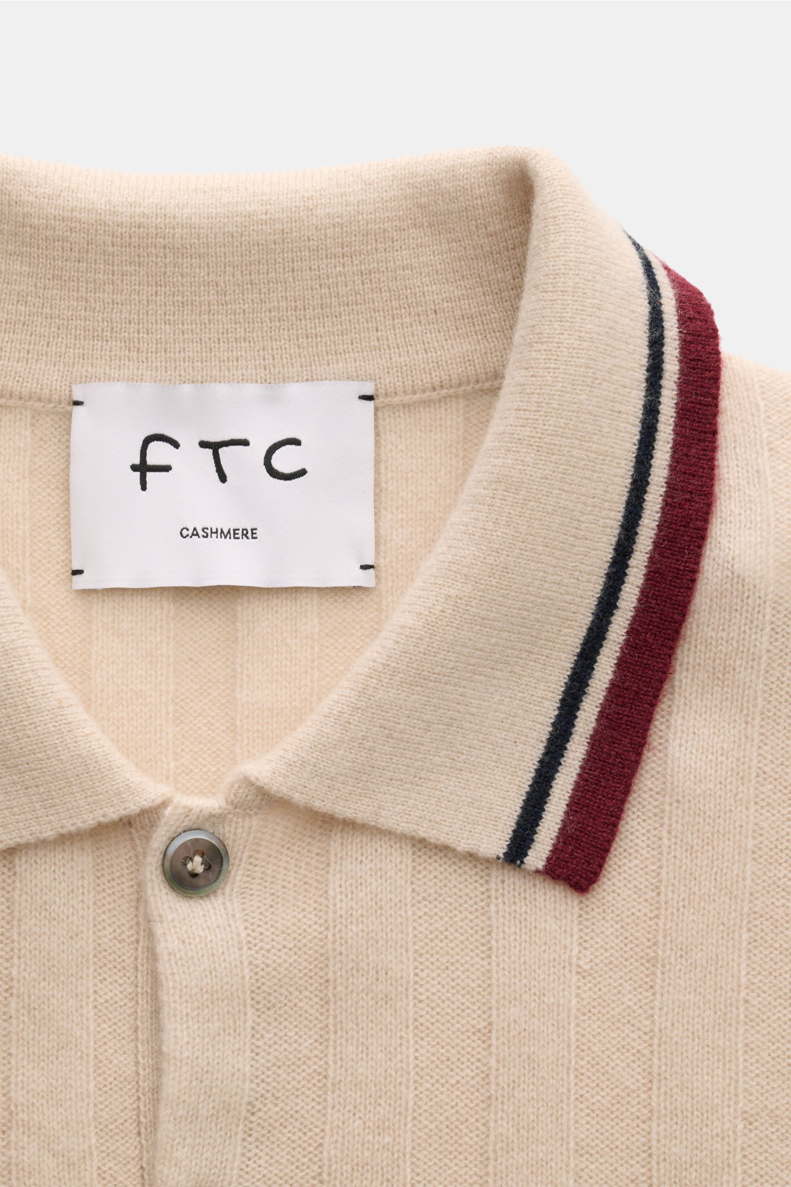 Nahaufnahme von FTC Cashmere Kurzarm-Strickpolo beige mit breitem Rippstrick, farblich abgesetzten Streifen am Polokragen und zwei Knöpfen.