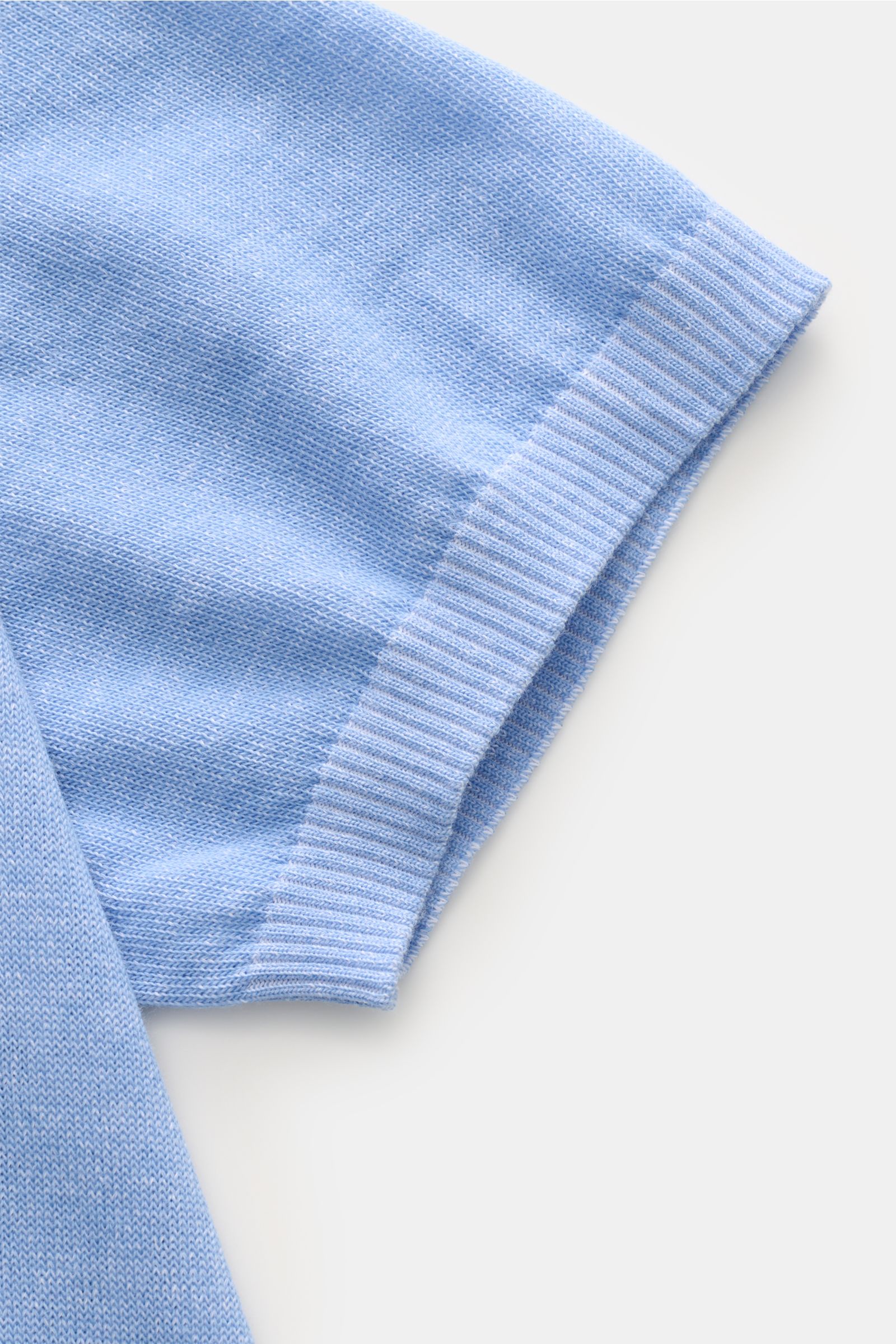 Close-up, top-down view of the sleeve of the Moorer Kurzarm-Strickpolo 'Coty' hellblau meliert, showing soft, fine-knit cotton fabric with ribbed cuff. Mehr als ein Basic: Für das Strickpolo 'Coty' kombiniert MOORER gekämmte Baumwolle mit Baumwoll-Crêpe, 
