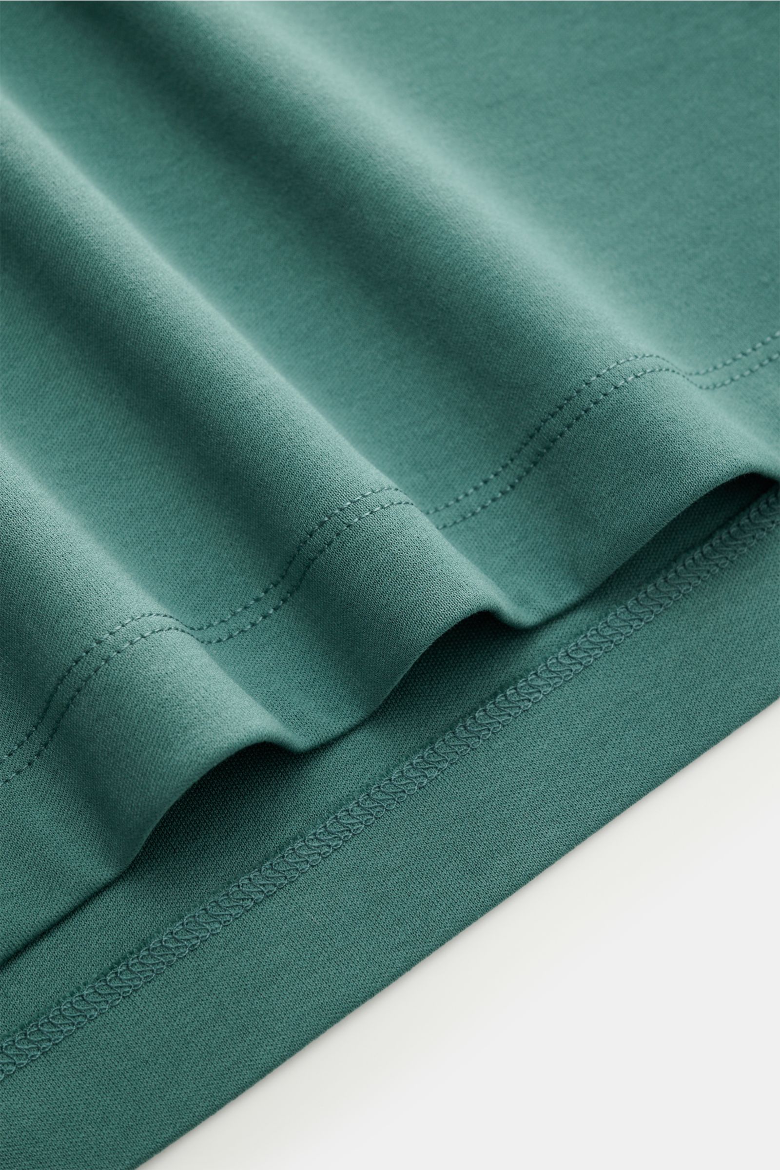 Nahaufnahme des Aurélien Jersey Poloshirts graugrün von unten fotografiert, zeigt feinen Jersey-Stoff aus ägyptischer Baumwolle, glatte Oberfläche mit Saumnaht und kurzen Saumschlitzen.