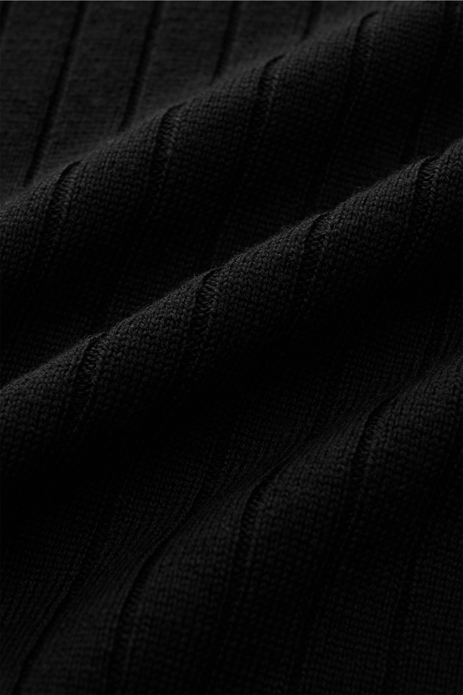 Nahaufnahme des Aurélien Merino Kurzarm-Strickpolo schwarz aus feinem Merinowoll-Rippstrick, weicher Griff, Slim Fit, Polokragen mit offener Kragenleiste und Rippbündchen, Detailansicht der Struktur.