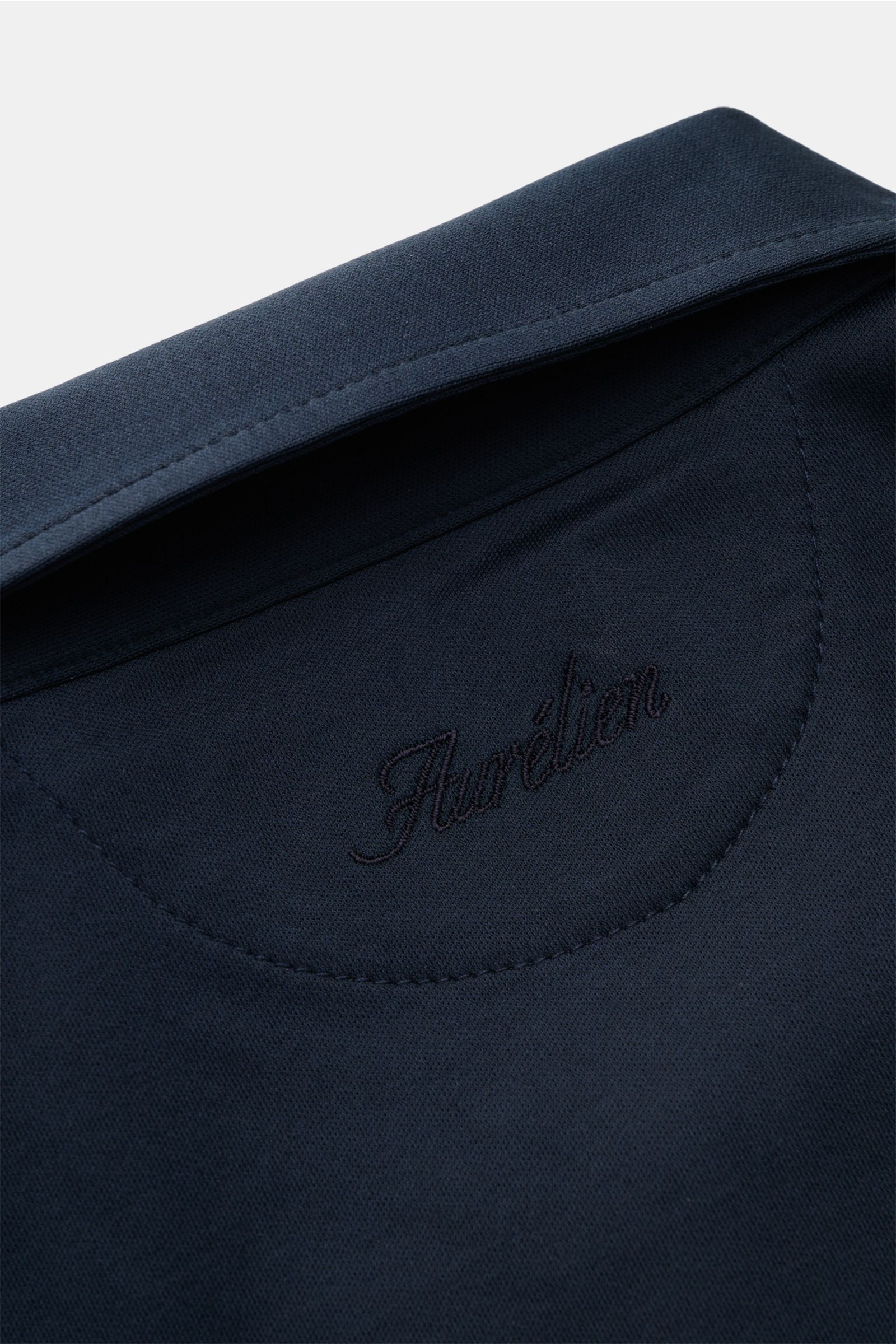 Close-up back view of the Aurélien Jersey-Poloshirt navy showing the embroidered logo and smooth fabric texture, made of pure cotton with a cool, smooth touch, slim fit, tailored polo collar, three-button placket, and short hem slits, a versatile basic fo