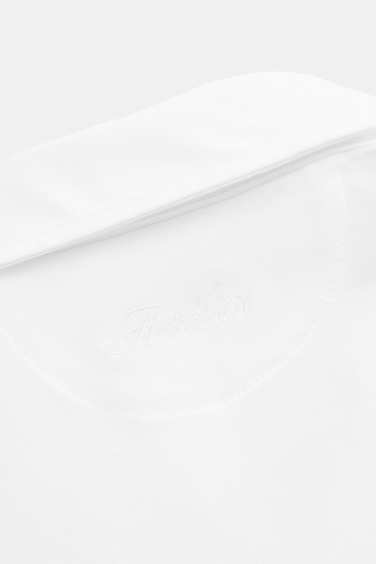 Close-up of the back collar area of the Aurélien Jersey-Poloshirt weiß, photographed from above, showing the embroidered brand name and smooth white cotton fabric, a versatile basic for spring and summer made of long-staple Egyptian cotton with a slim fit