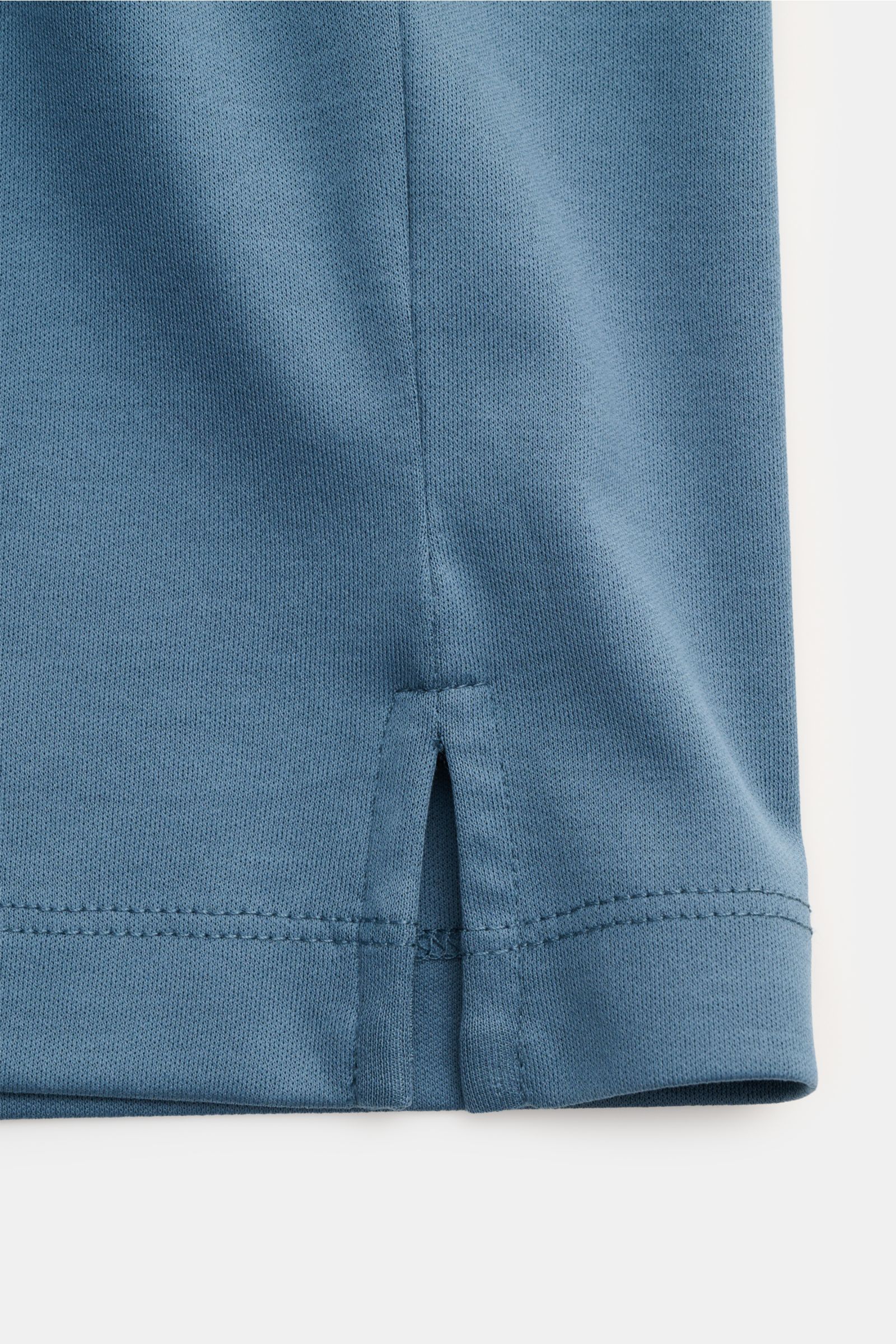 Close-up image of the lower hem of the Aurélien Jersey-Poloshirt petrol, photographed from the side to show the short side slit and neat stitching. Vielseitiges Basic für den Frühling und Sommer: Das Jersey-Poloshirt von AURÉLIEN verbindet langstaplige, ä