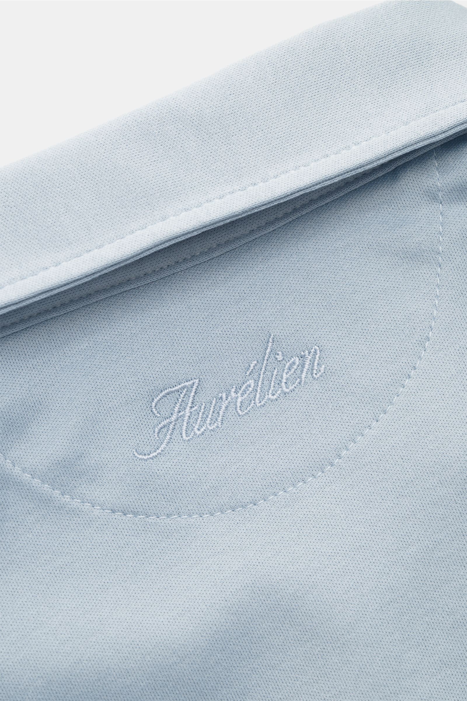 Close-up image of the Aurélien Jersey-Poloshirt hellblau collar from above, showing light blue fabric and embroidered logo. Vielseitiges Basic für den Frühling und Sommer: Das Jersey-Poloshirt von AURÉLIEN verbindet langstaplige, ägyptische Baumwolle mit 